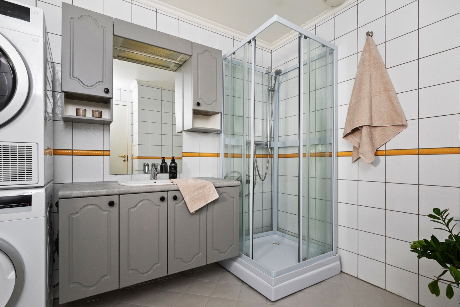 Baderomsinnredningen har grå, profilerte fronter og består av en nedfelt servant på en skuffeseksjon, to veggskap og et speil med belysning. Galleribilde