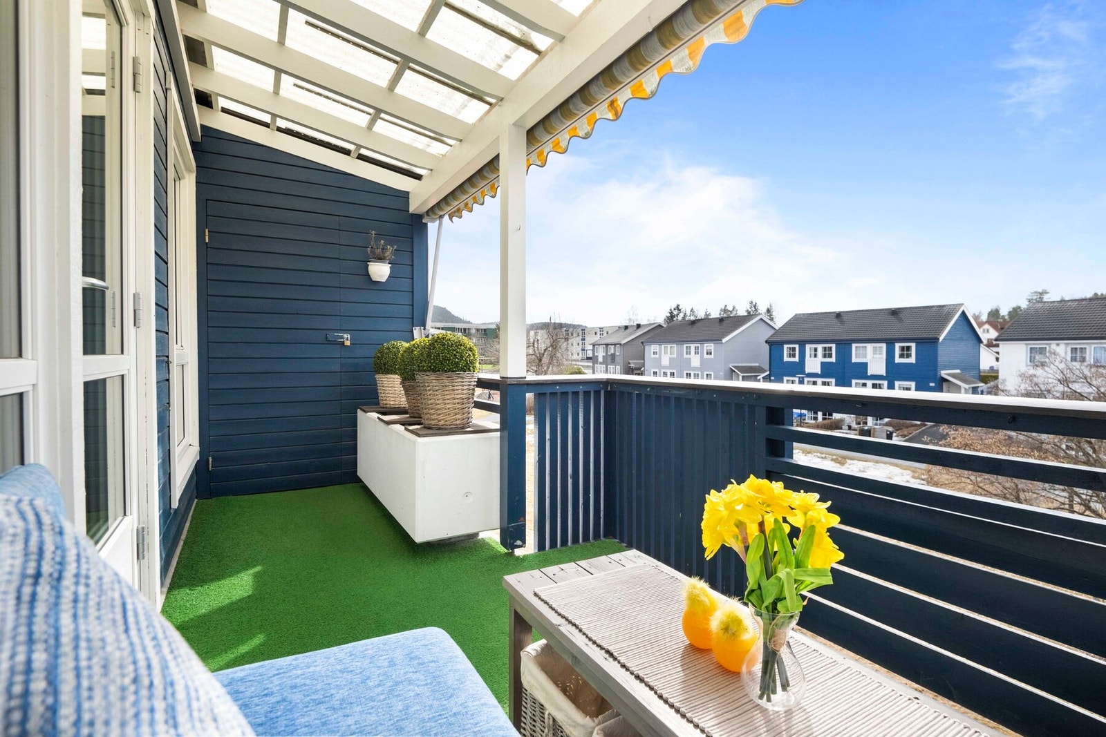 Balkongen har overbygg med takplate, montert markise og gulv belagt med gressmatte i plast. Galleribilde