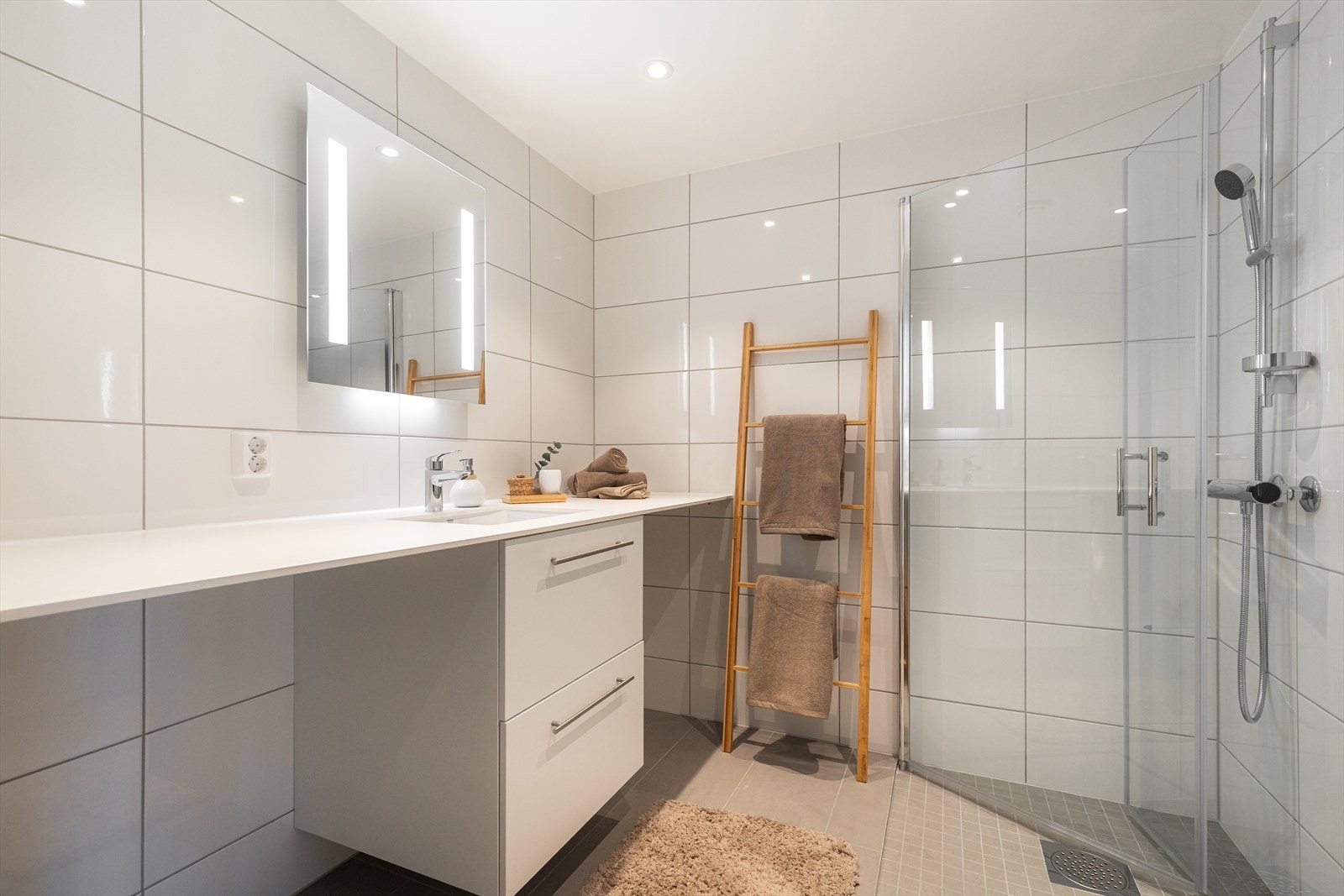 Delikat og flislagt baderom med varmekabler på gulv. Vaskemaskin og tørketrommel kan enkelt og plassbesparende plasseres under heldekkende benkeplate Galleribilde