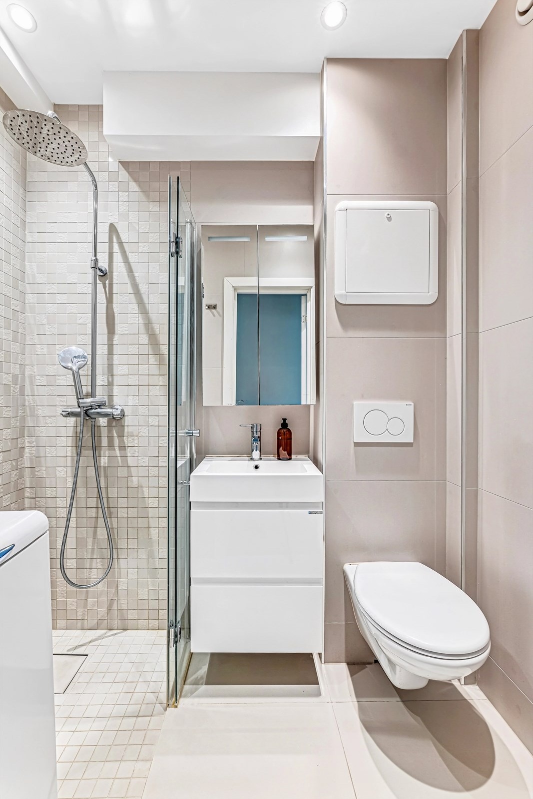 Rommet er innredet med servant på innredning, speilskap, dusjhjørne med innfellbare glassører, vegghengt toalett og opplegg for vaskemaskin. Galleribilde