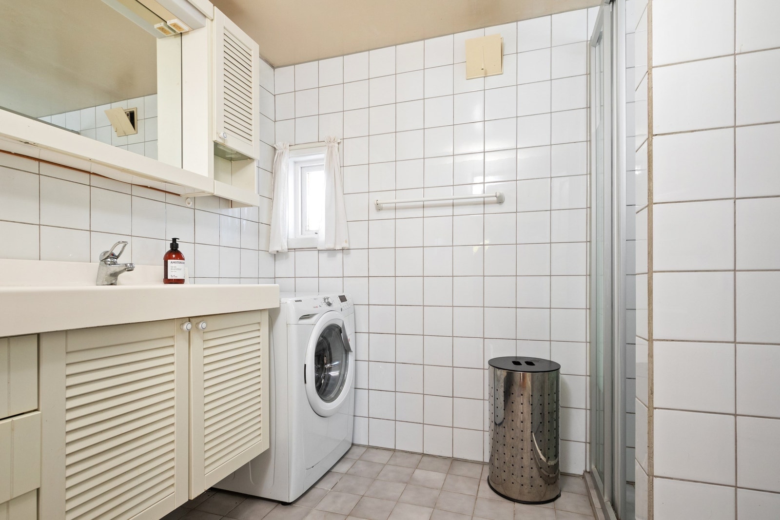 Fliser på gulv og vegg, malte slette plater i tak. Det er gulvmontert toalett og innredning med heldekkende servant, speil og speilskap. Dusjnisje med glassdør. Skyllekar og opplegg for vaskemaskin. Galleribilde