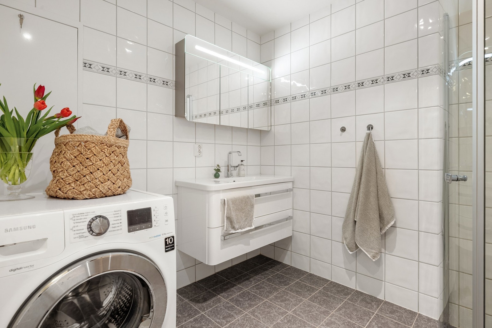 Badet er helfliset og har innfelte downlights i himling. Innredningen består av vegghengt toalett, opplegg for vaskemaskin, dushjørne og baderomsinnredning. Galleribilde