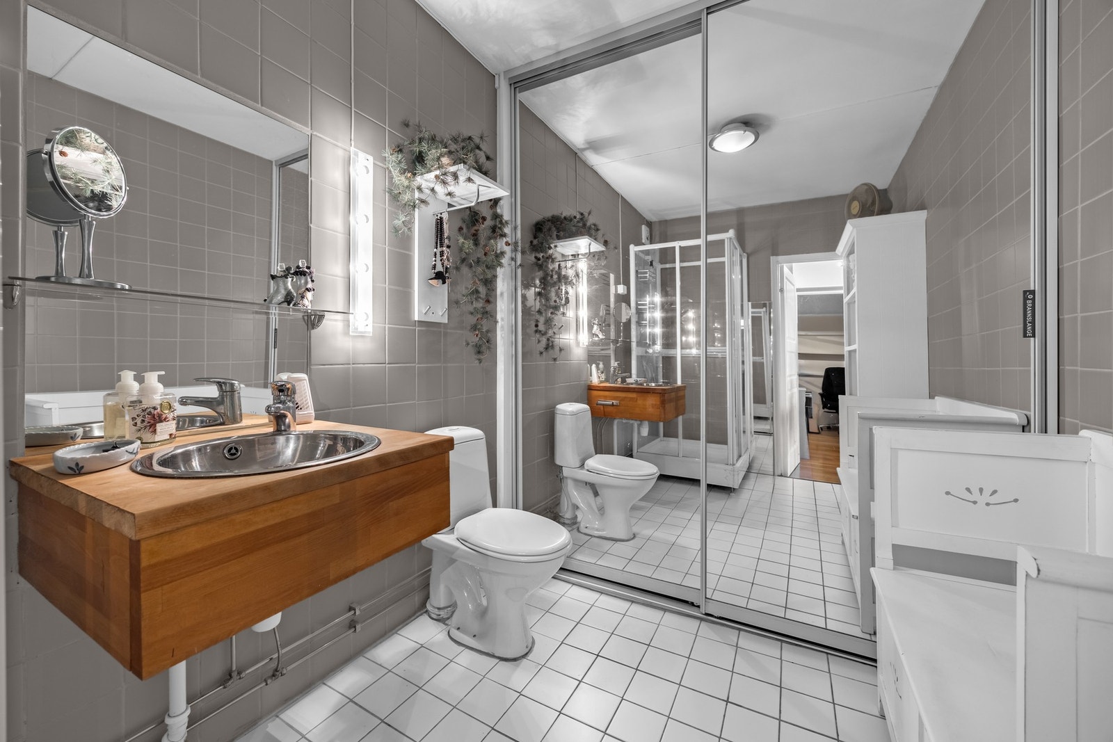 Tidløst bad i flislagt utførelse med opplegg for vaskemaskin og lagring bak skyvedørsgarderobe. Galleribilde