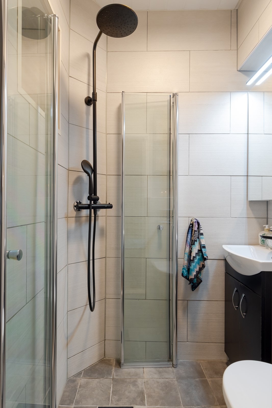 Dusjhjørne med sammenleggbare glassdører, samt dusjarmatur tilkoblet hånddusj og regndusj, gir fleksibilitet og komfort. Vaskemaskin er plassert på kjøkkenet. Galleribilde