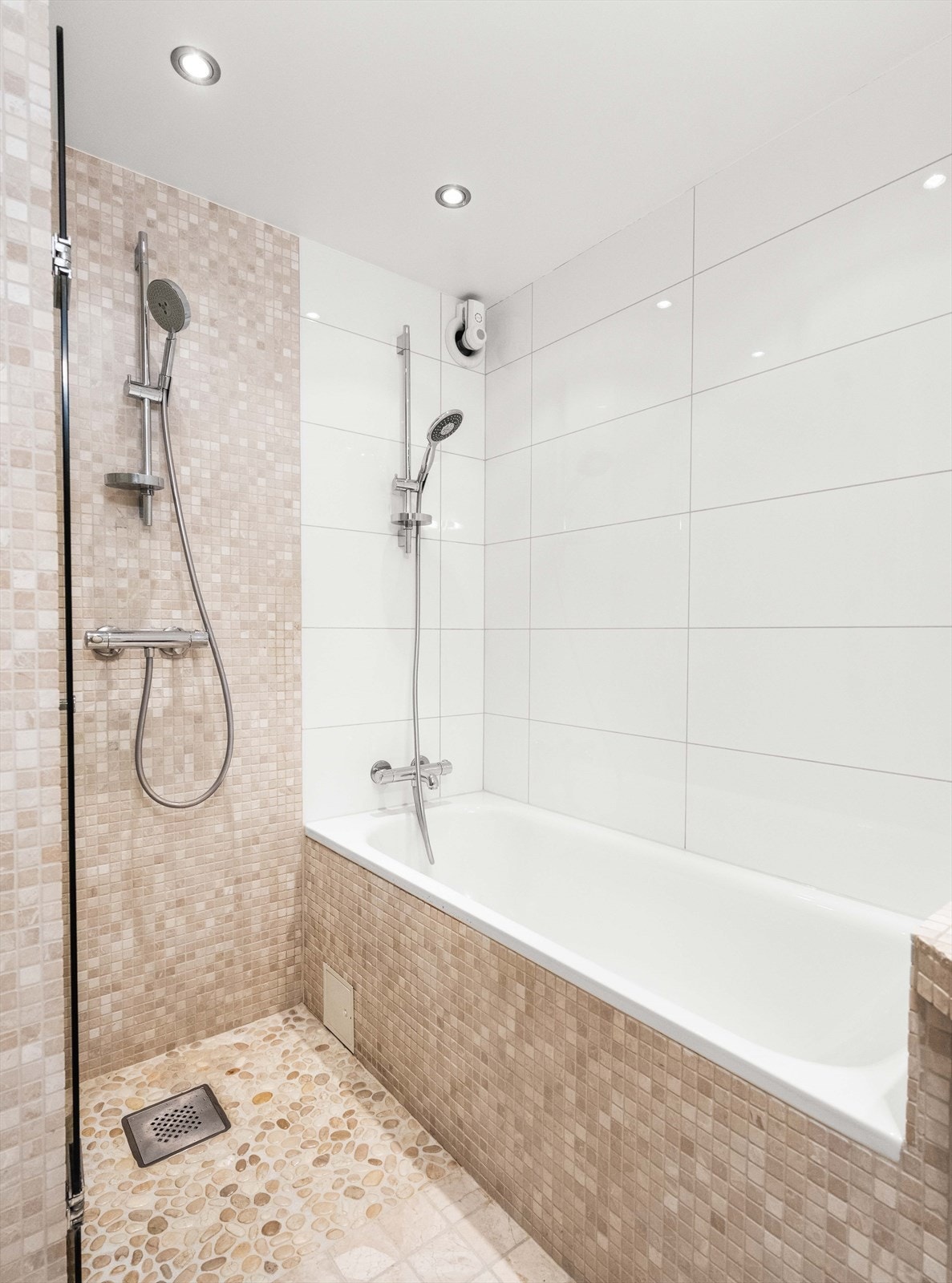 Dusjen er på gulv i hjørnet og har dusjbatteri tilkoblet veggmontert hånddusj. Badet har også innmurt badekar. Galleribilde