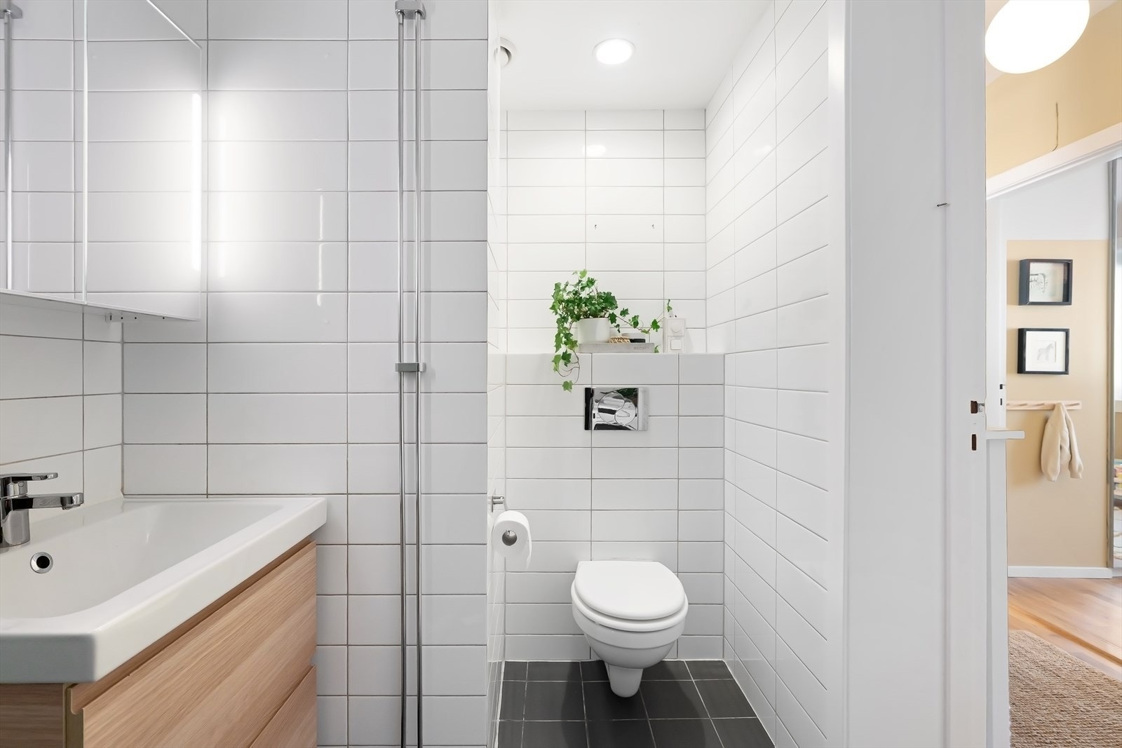 Delikat flislagt bad med varmekabler i gulv og moderne innredning med underskap og speilskap med belysning over Galleribilde