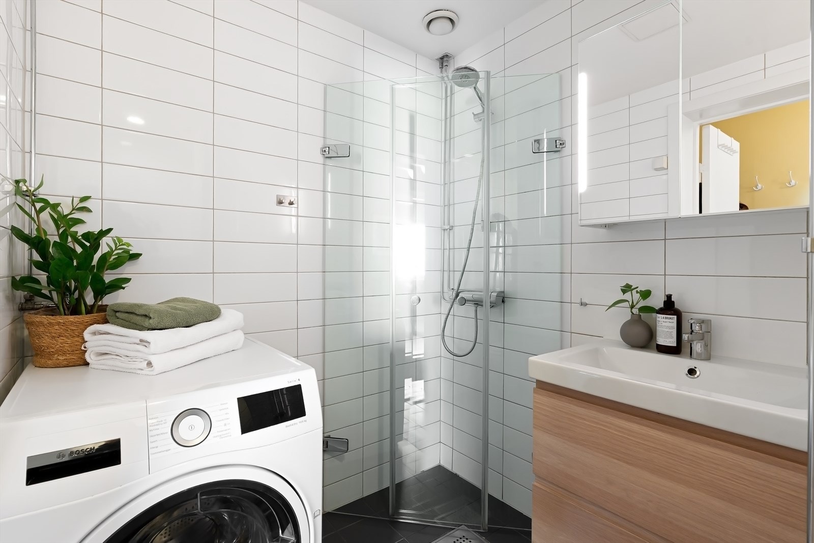 Badet er utstyrt med naturlig avtrekk, dusjhjørne med glassdører og armatur, vegghengt wc og opplegg for vaskemaskin Galleribilde