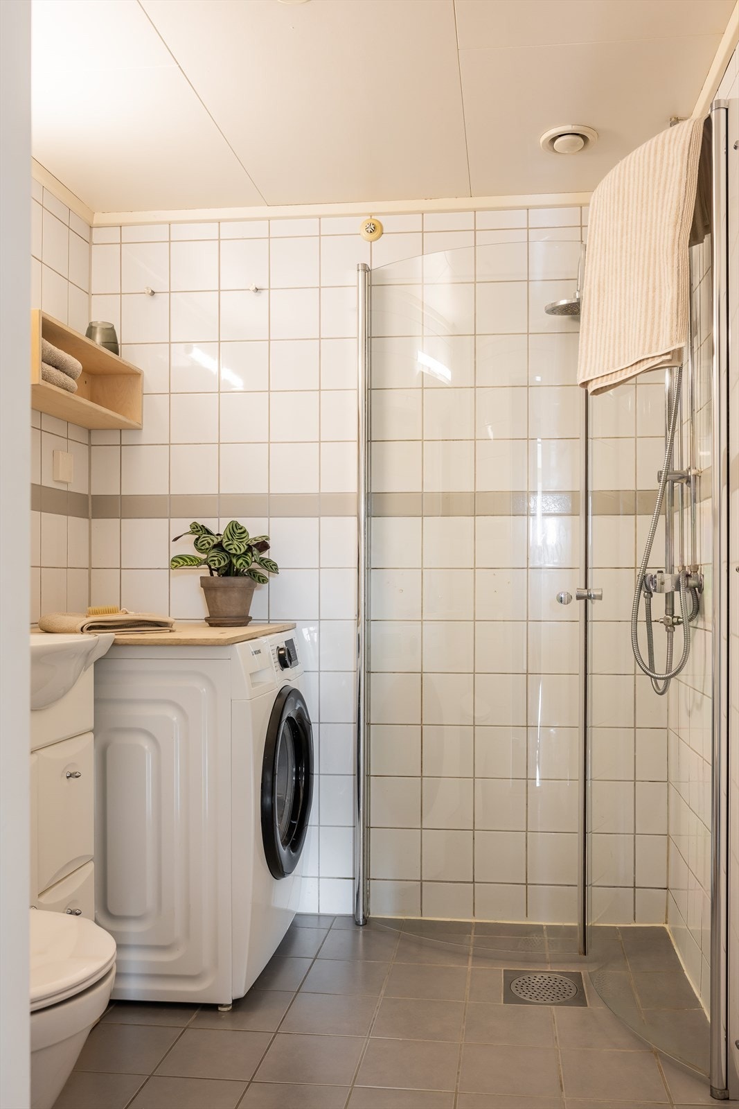 Videre har badet dusjhjørne med innfellbare glassdører og gulvstående toalett. Det er opplegg for vaskemaskin. Galleribilde