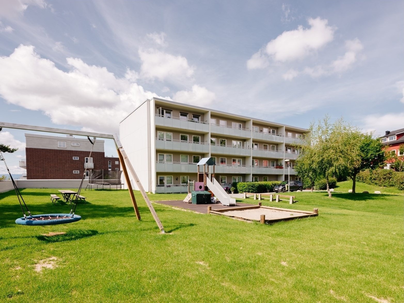 Svært romslig bakgård med lekestativ, huske, trampoline og sittegrupper Galleribilde