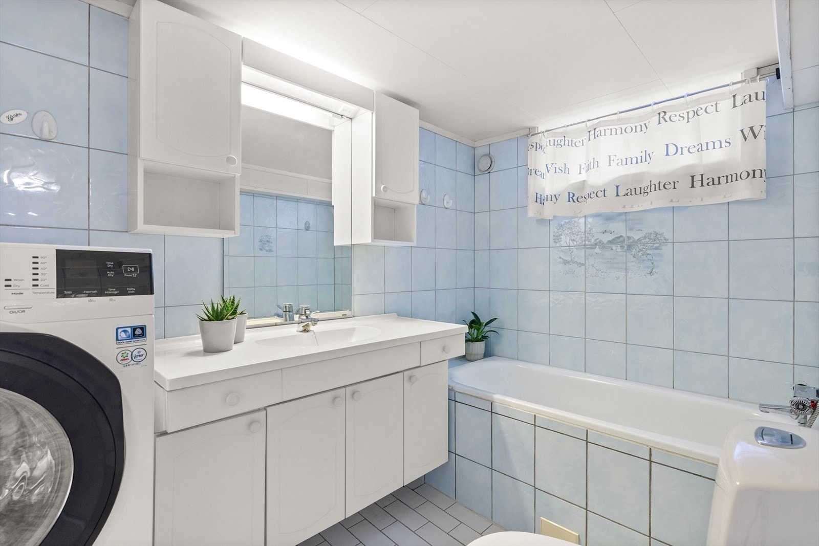 Flislagt bad/vaskerom i kjeller med varmekabler i gulv. Rommet består av innmurt badekar, opplegg for vaskemaskin, innredning med servant, speil og overskap. Galleribilde