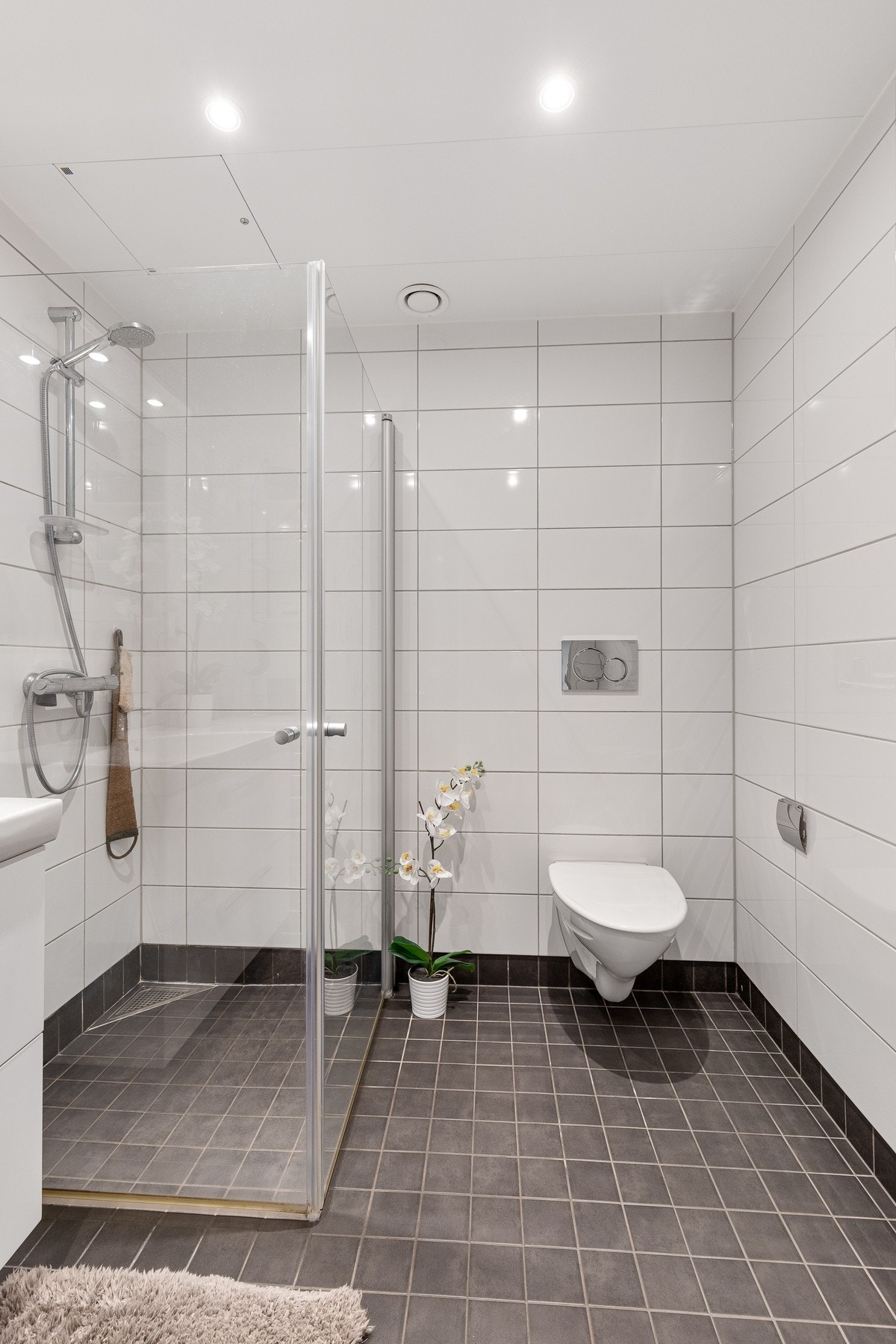 Badet er av god størrelse og består av servant med underskap, belyst speil, vegghengt WC og dusjsone med innfellbare dusjdører Galleribilde