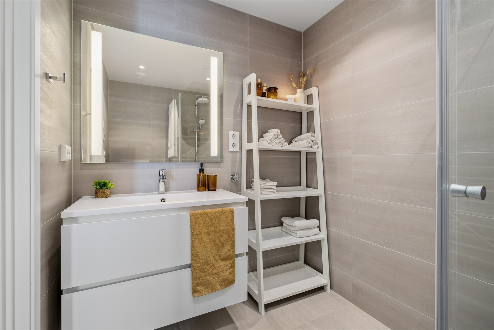 Den nedfelte servanten er plassert i en stilren baderomsinnredning med gode oppbevaringsmuligheter. Veggmontert toalett gir et ryddig uttrykk og forenkler renholdet, mens dusjsonen er avgrenset med elegante dusjvegger som skaper en følelse av romslighet. Galleribilde