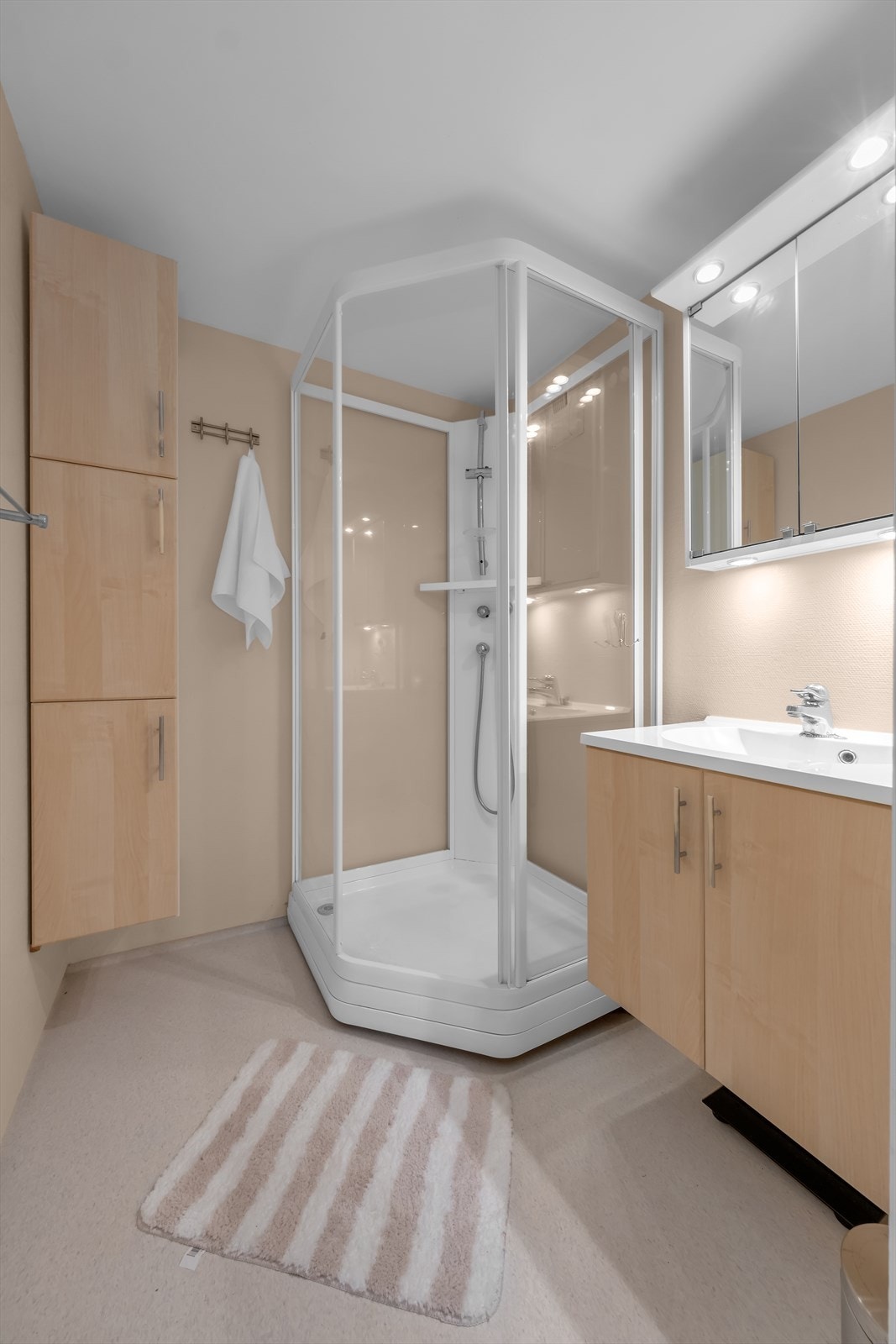 Lyst bad med belegg på gulv med varmekabler og malte tapetserte vegger. Innredet med dusjkabinett og baderomsinnredning med servan Galleribilde