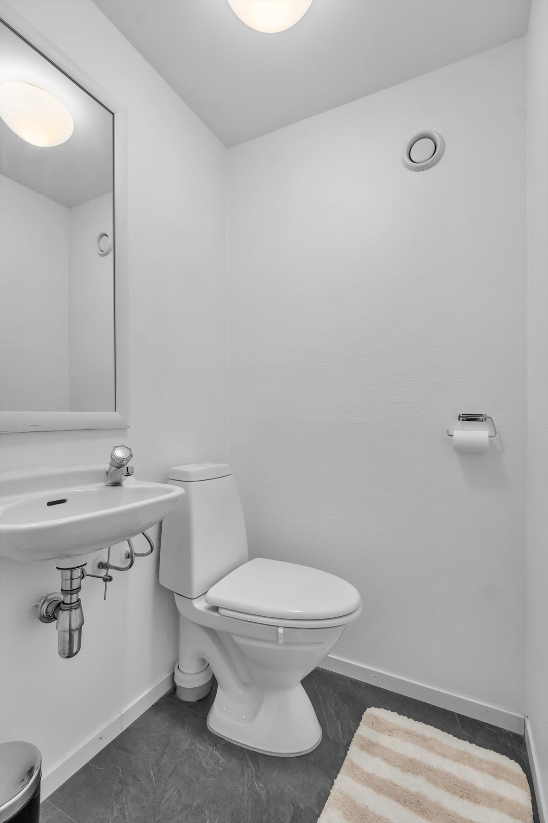 Toalettrom med laminat på gulv og lyse tapetserte vegger. Innredet med servant og toalett Galleribilde