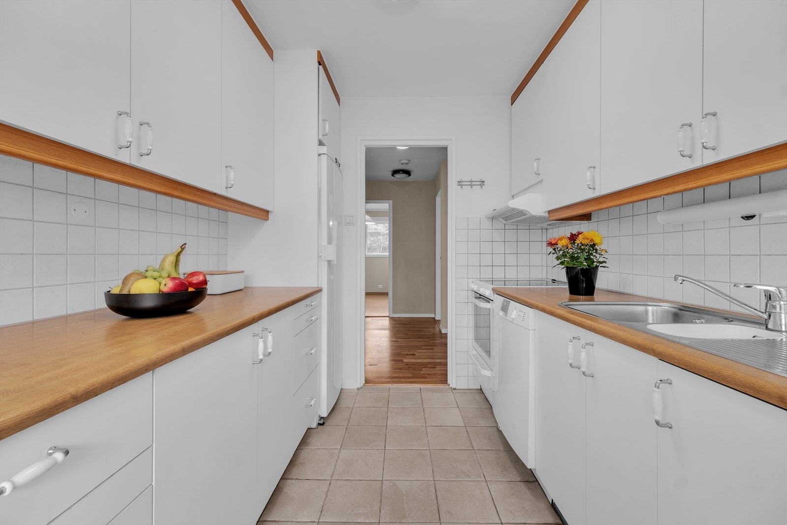 Kjøkkenet er innredet med frittstående hvitevarer med komfyr, oppvaskmaskin og kjøleskap Galleribilde