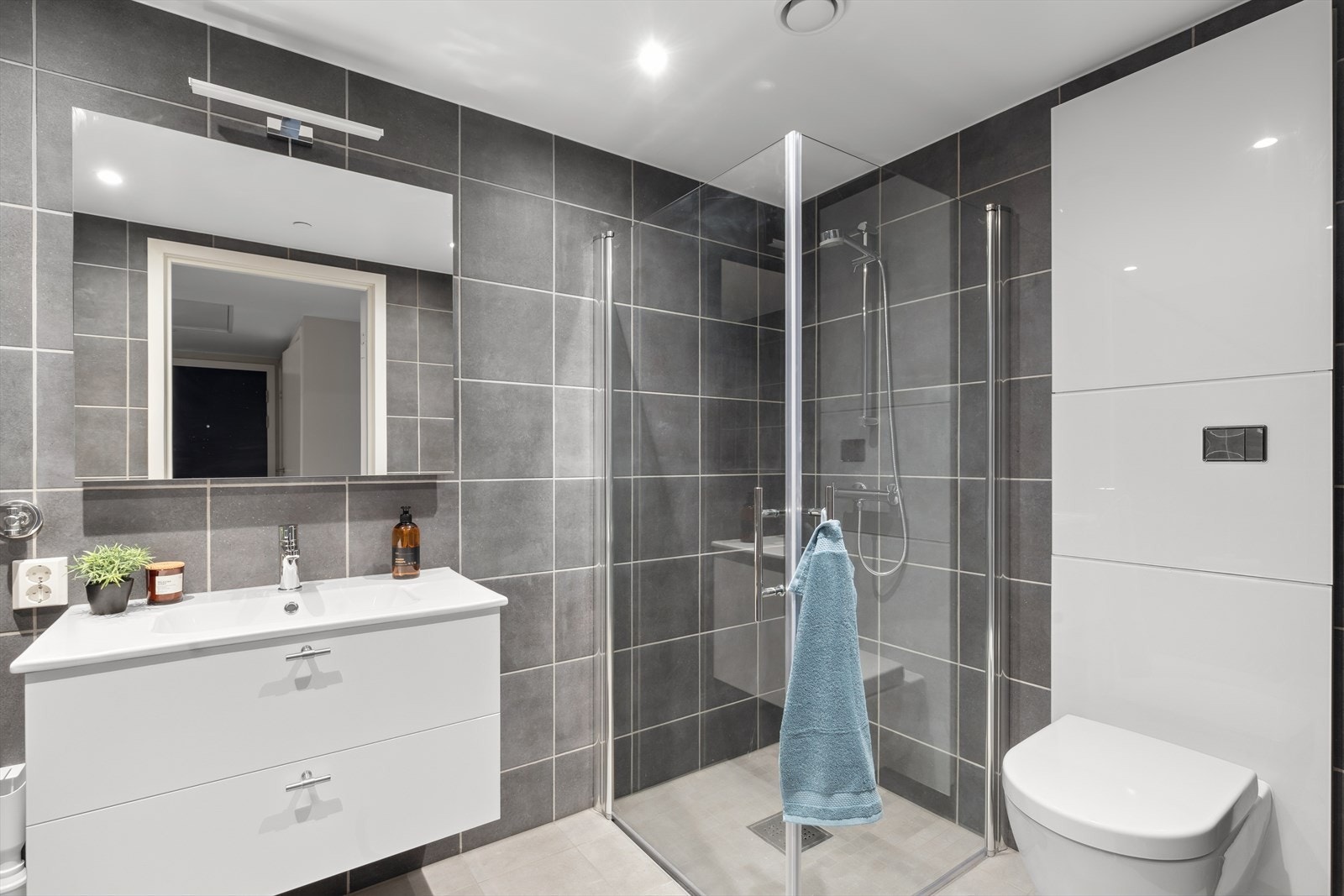 Badet er utstyrt med vegghengt toalett, dusjhjørne med svingbare glassdører, baderomsinnredning med heldekkende servant, samt opplegg for vaskemaskin. Galleribilde