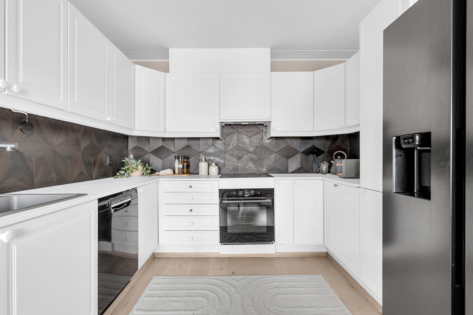 Innredningen består av hvite, profilerte fronter i klassisk stil. Benkeplaten er i hvit laminat, og ble sammen med servant og kitchenboard oppgradert i 2021. Galleribilde