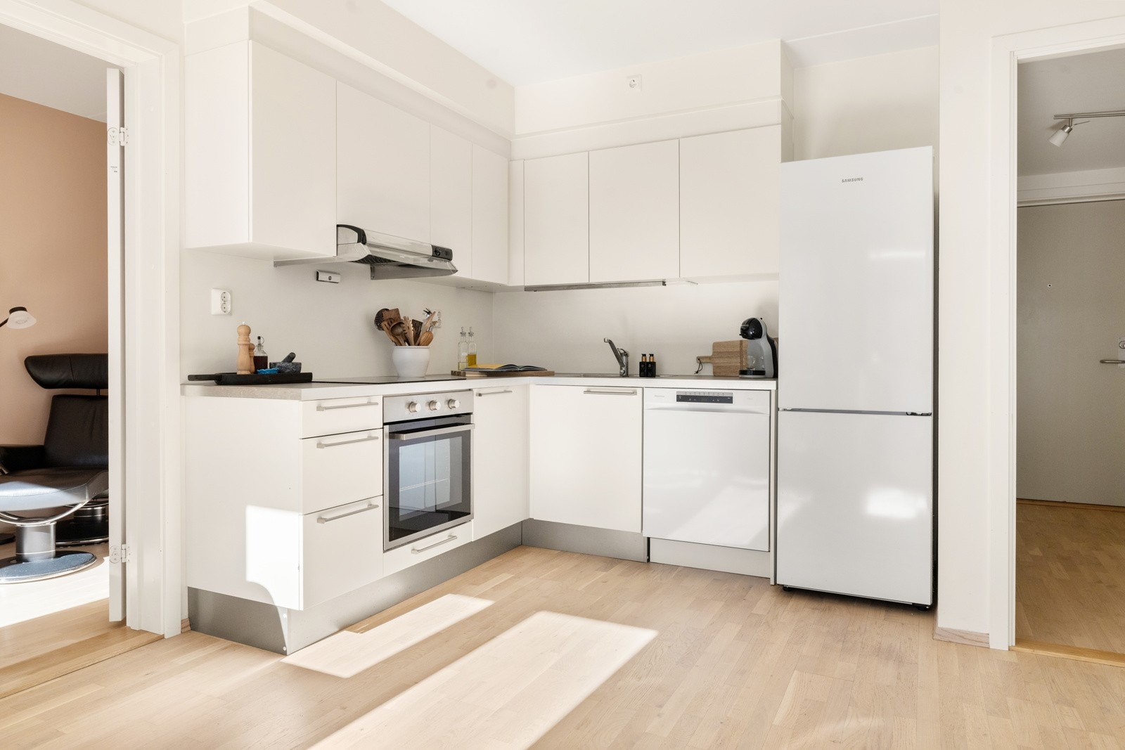 Tidløs kjøkkeninnredning montert langs to av veggene med hvite, glatte fronter. Galleribilde