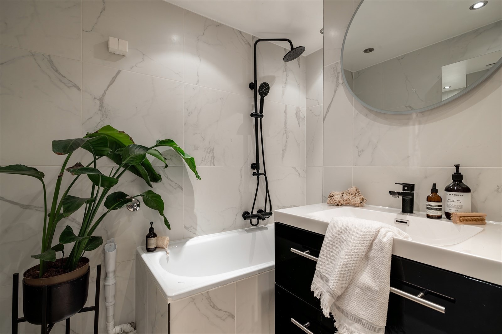 Badet er flislagt på gulv og vegger, med innredning som inkluderer servant med underskap, speil med lys, veggskap og badekar med dusjløsning. Galleribilde