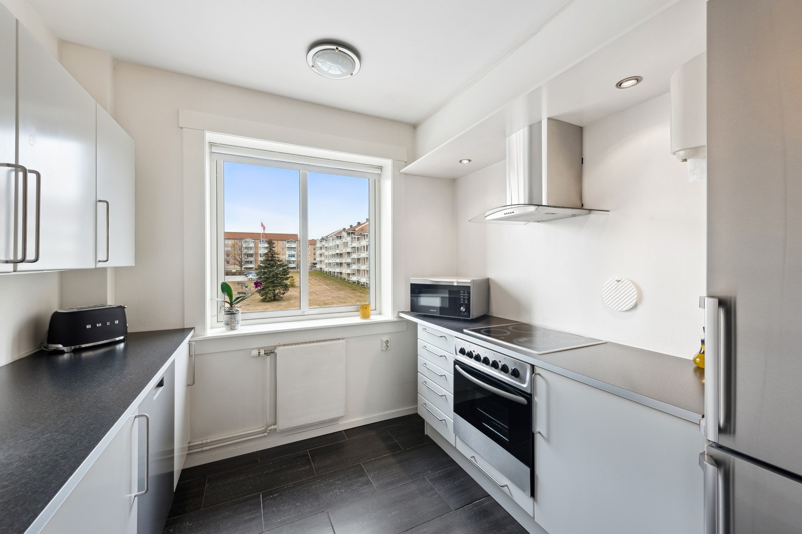 Kjøkkeninnredning med slette fronter, laminat benkeplate. Benkebelysning og stikkontakter under overskap. Galleribilde