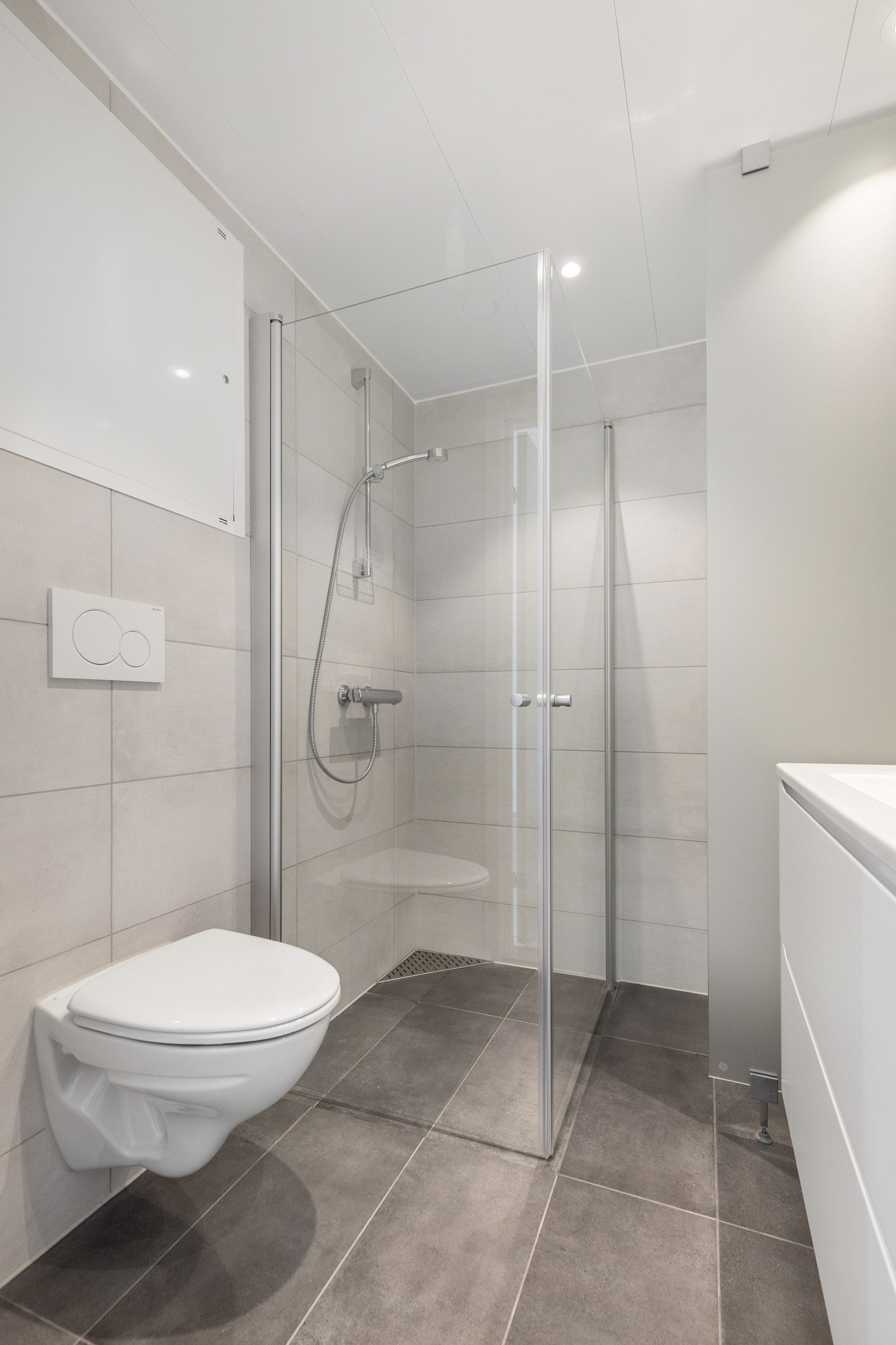 Badet er utstyrt med downlights, servant m/lagring, dusjhjørne, vegghengt wc og opplegg for vaskemaskin. Galleribilde