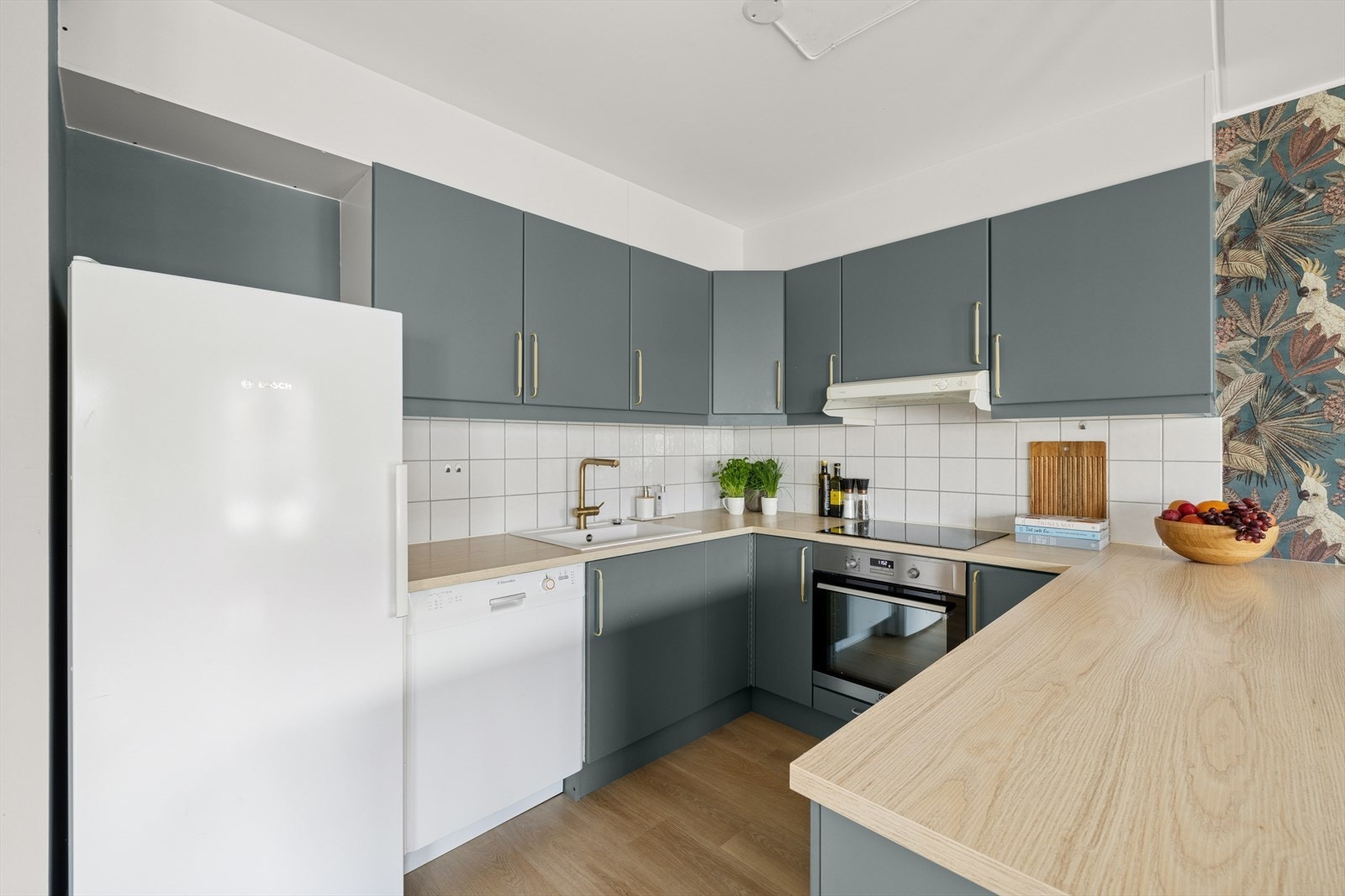 Kjøkkenet er i glatte malte fronter med fliser på vegg. Integrert platetopp og stekeovn med plass til kjøl/frys og opplegg for oppvaskmaskin. Galleribilde