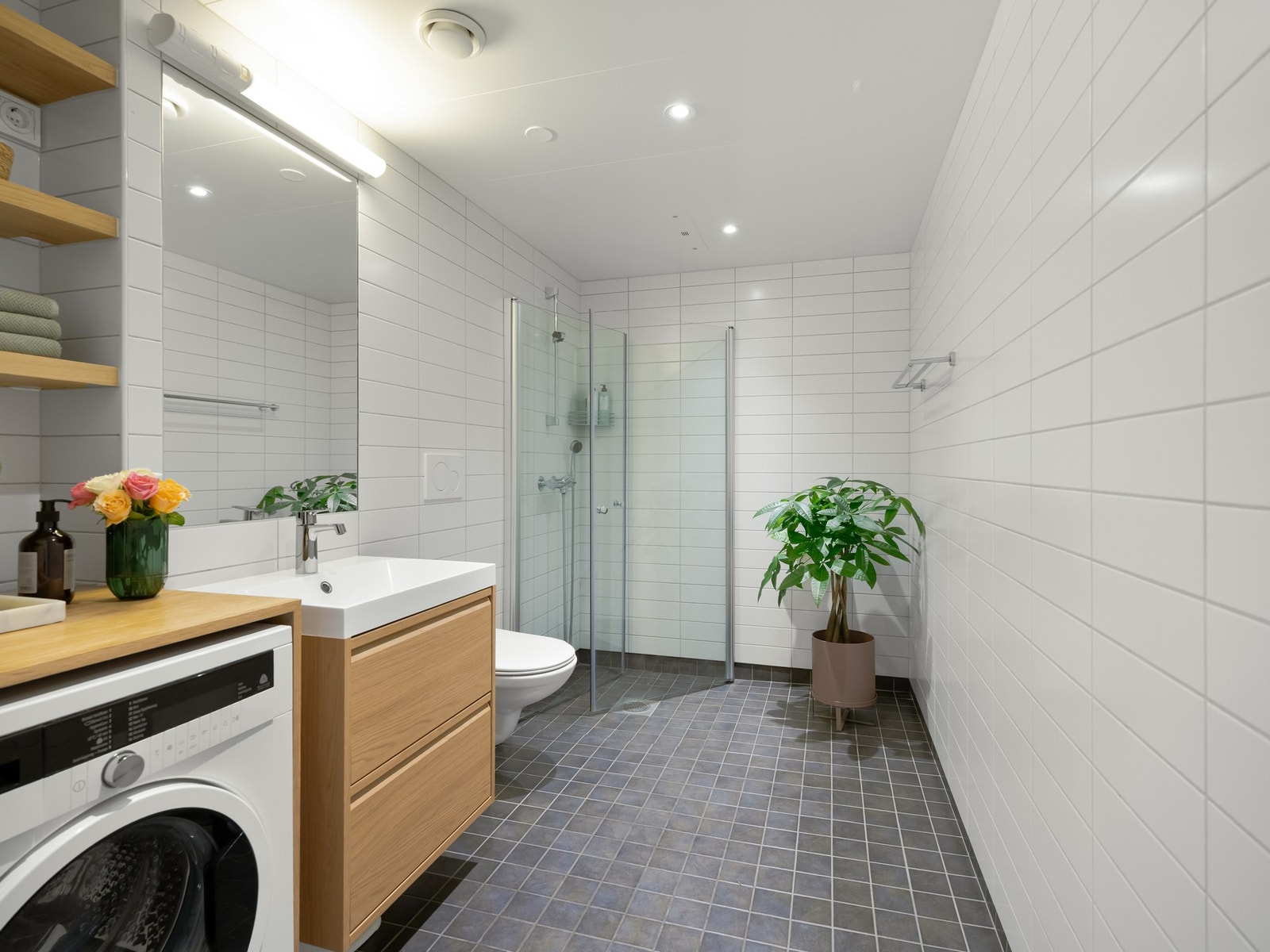 Badet er pent flislagt og fra byggeår 2017. Det er innredet med dusjsone med innfellbare glassdører, servantskap (nytt i 2025), speil på vegg og hylle i overkant av vaskemaskinen. Galleribilde