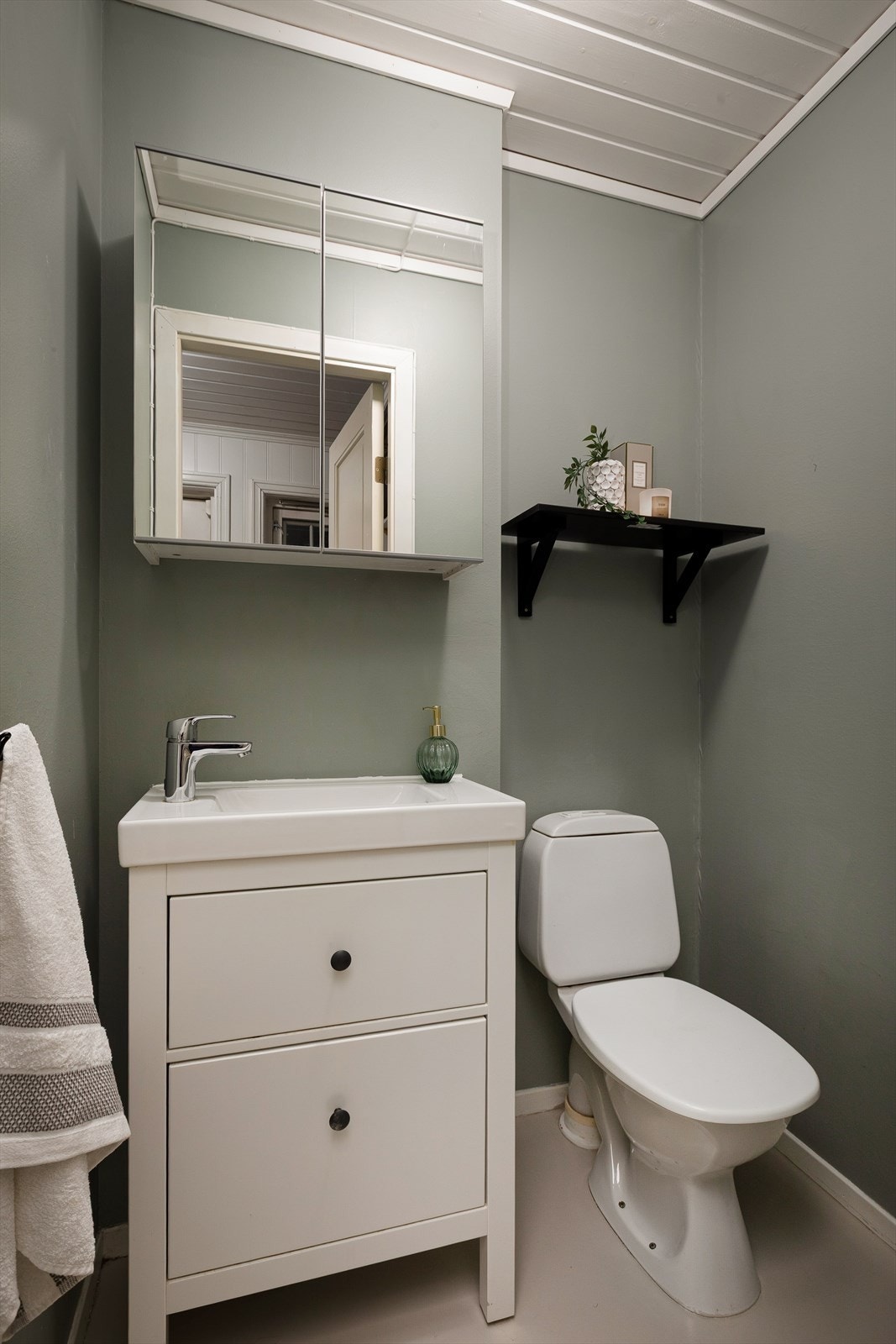 Toalettrommet i første etasje er utstyrt med servant, speilskap og et moderne toalett som ble oppgradert i 2019. De malte veggene i en dempet grønnfarge gir et lunt inntrykk. Galleribilde