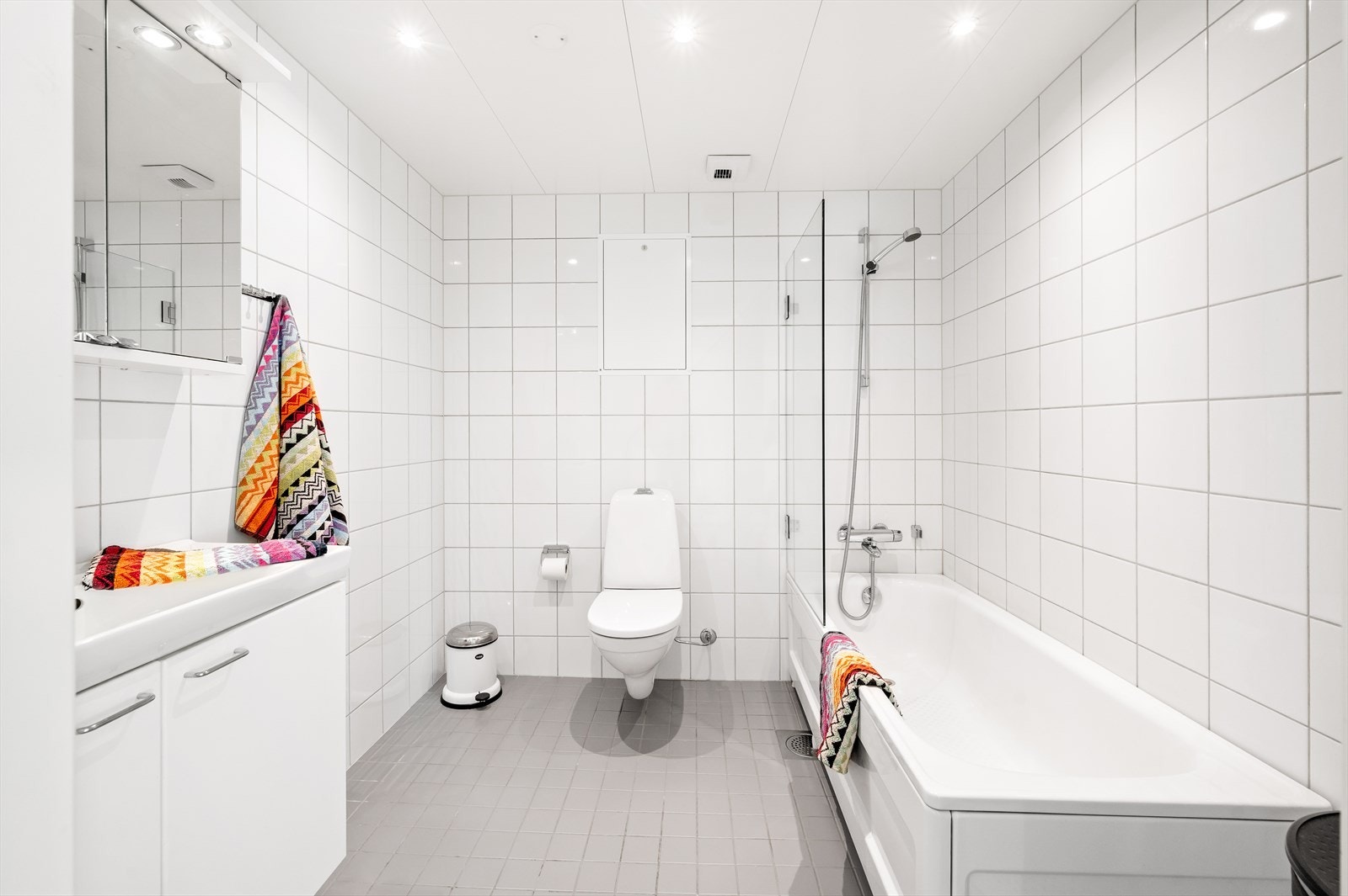 Leiligheten har to stilige, moderne bad, begge med inngang fra gangen ved soverommene. Dette badet har veggmontert toalett med utenpåliggende sisterne og badekar med dusjvegg i glass. Galleribilde