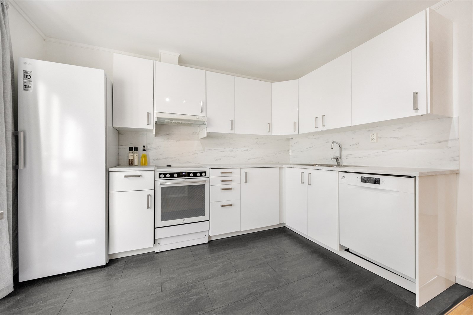 Kjøkkenet inneholder laminat benkeplate med nedfelt oppvaskkum, laminatplater på vegg over benkeplate, og nisjer for komfyr, oppvaskmaskin og kjøl-/fryseskap. Galleribilde