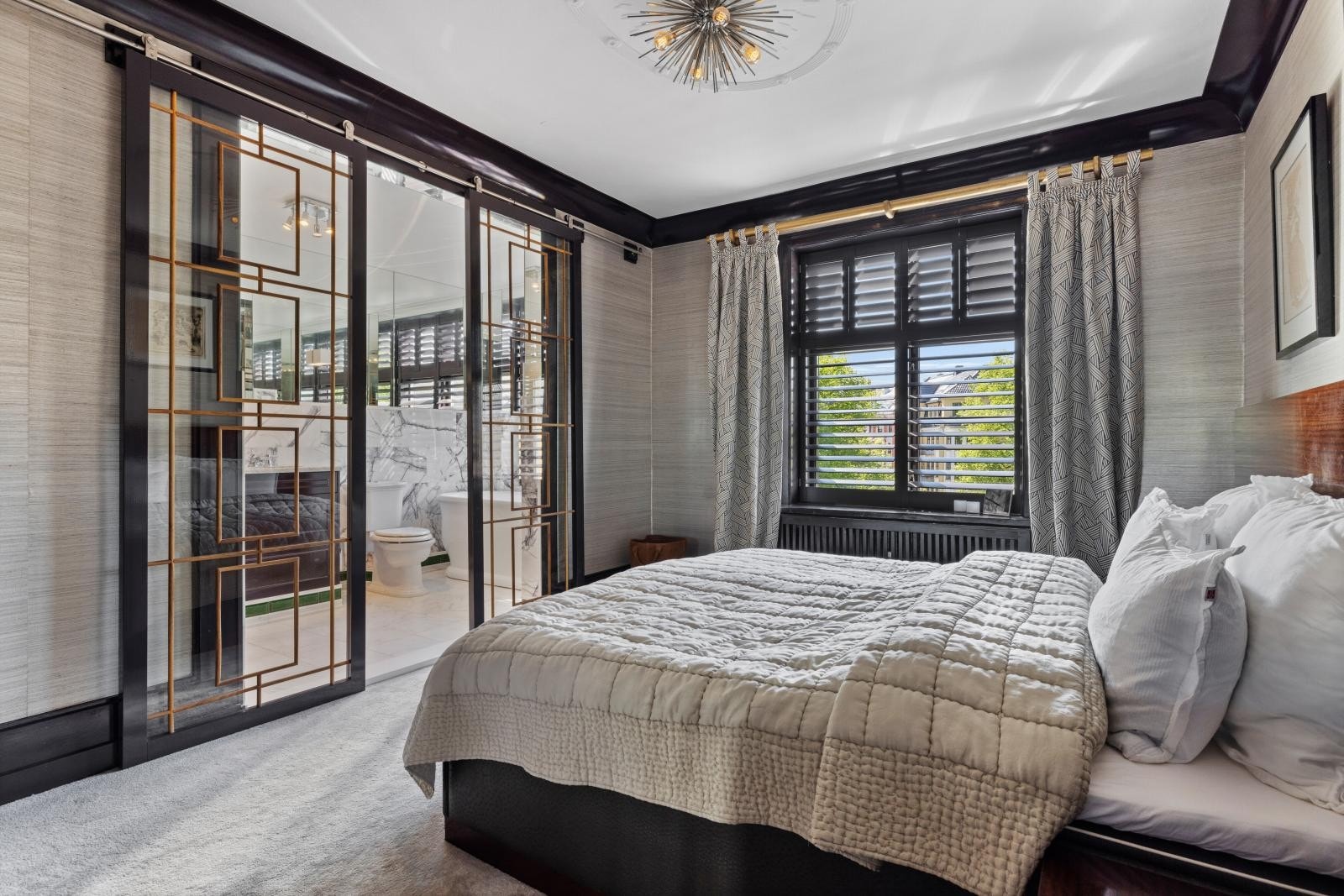 Master soverom. Et en suite-baderom skilles fra soverommet med utenpåmonterte skyvedører med art deco-sprosser Galleribilde