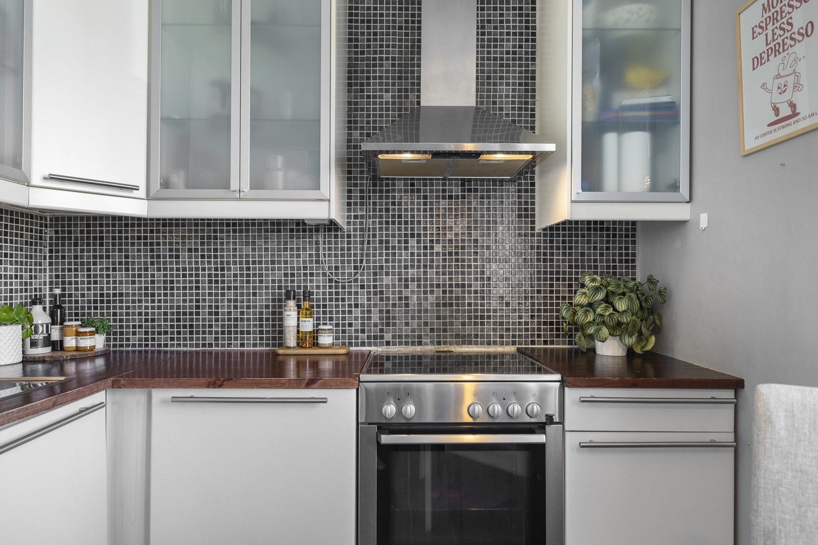 Det er god plass til å innrede med frokostbord i tilknytning til kjøkkenet. Overskapene er hvite med en kombinasjon av slette fronter og glassfronter. Benkeplaten er i mørkt treverk, og veggen mellom over- og underskap er kledd med mosaikkfliser. Galleribilde