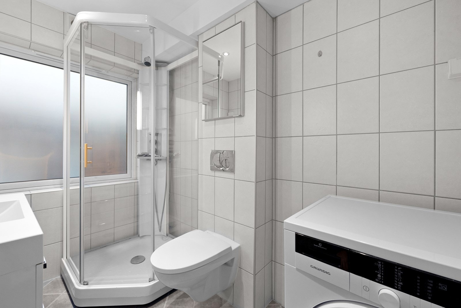 Badet er innredet med servant, veggmontert toalett, dusjkabinett og opplegg for vaskemaskin Galleribilde