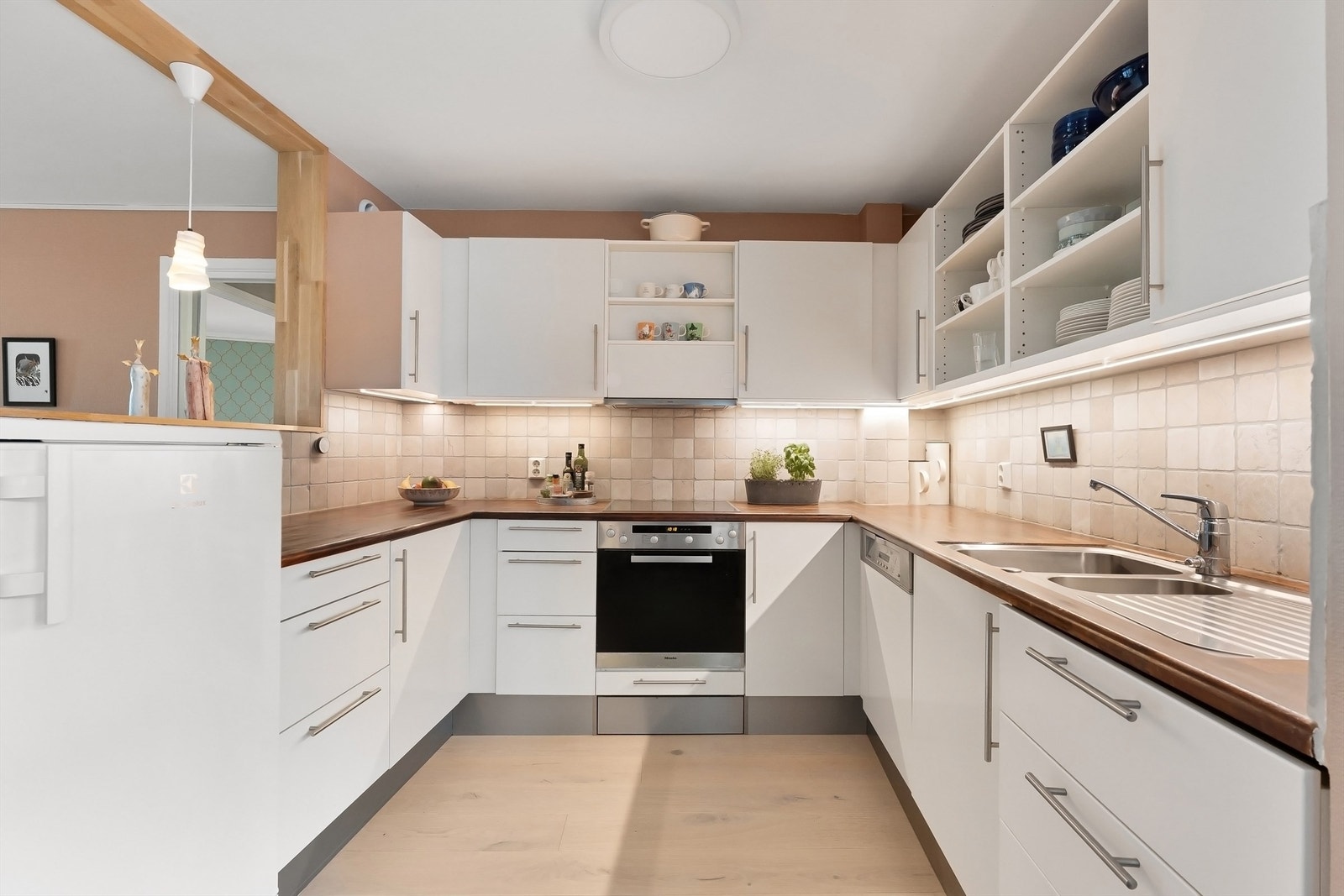 Kjøkkenet har slette fronter på skap og skuffer, benkeplater av treverk med nedfelt oppvaskkum og veggfliser over benkeplaten Galleribilde