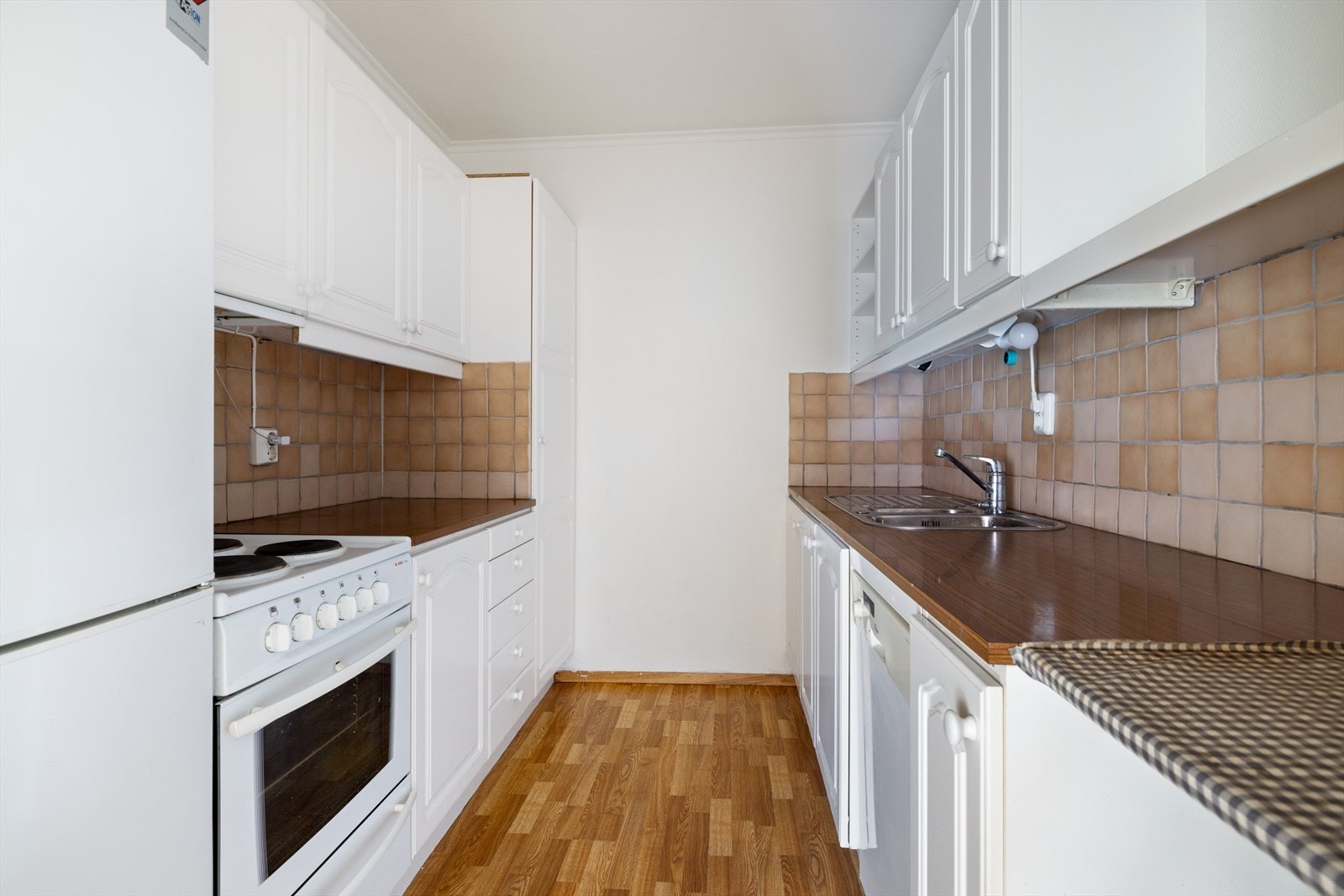 Kjøkkeninnredning med hvite profilerte fronter og laminert benkeplate med dobbel oppvaskkum i rustfritt stål Galleribilde