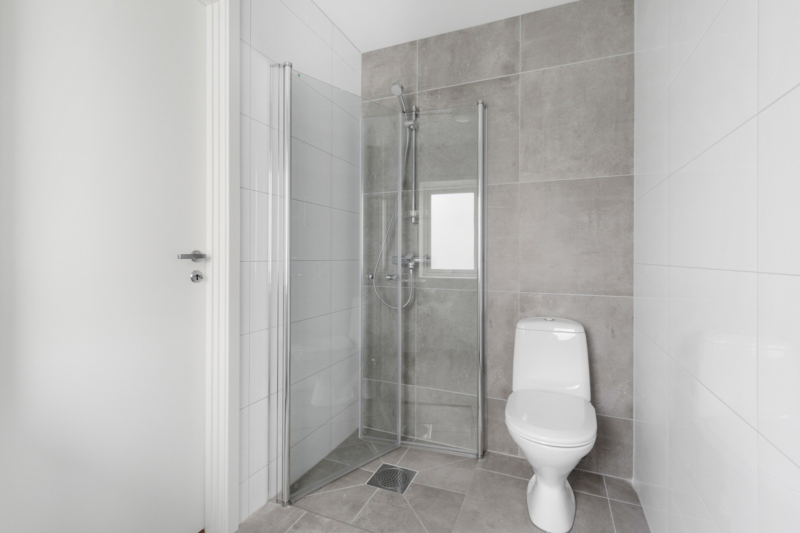 Det er speil, LED-overlys, servant på hvit skapinnredning, gulvmontert toalett og et dusjhjørne med innsvingbare glassdører. Rommet har opplegg for vaskemaskin og tørketrommel. Galleribilde