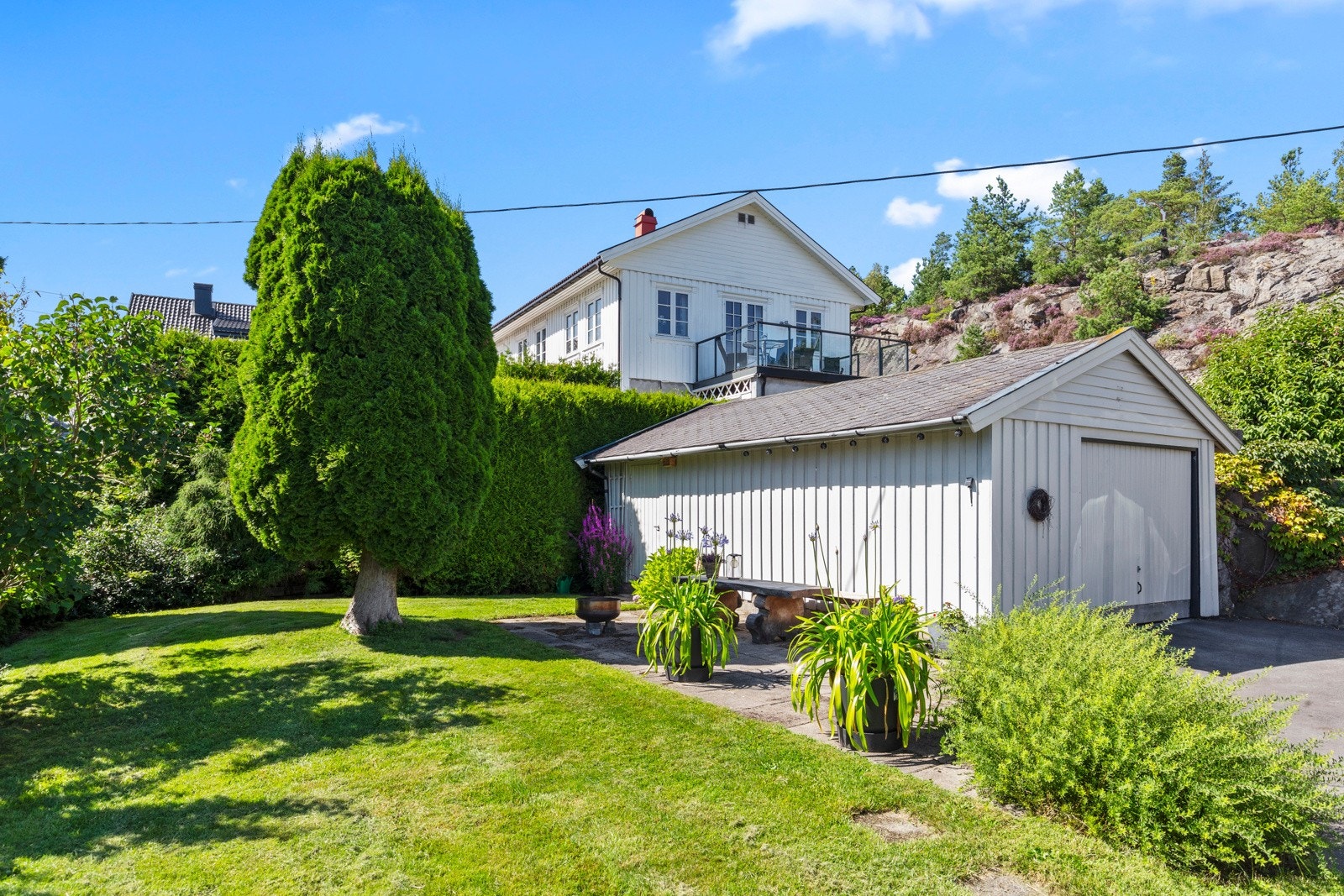 Ved en asfaltert gårdsplass finner man en frittliggende garasje med bod. Galleribilde
