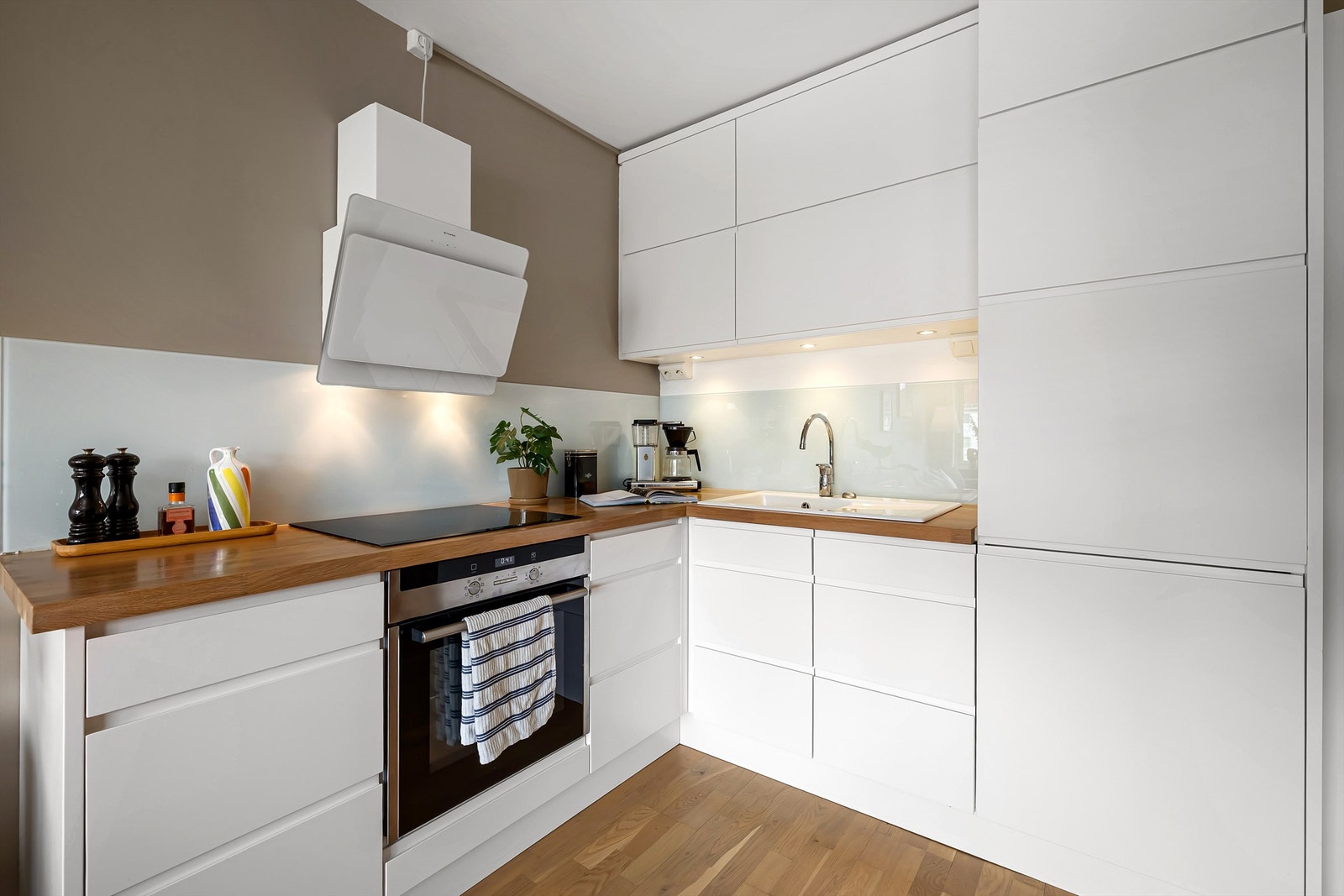 Kjøkkeninnredning med glatte fronter og benkeplate i tre med nedsenket oppvaskkum i porselen med to-greps armatur Galleribilde