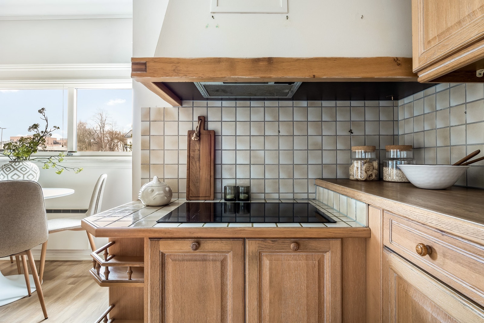 Benkeplater av laminat samt flislagt benk ved induksjonstopp og flislagte veggflater over kjøkkenbenker. Galleribilde