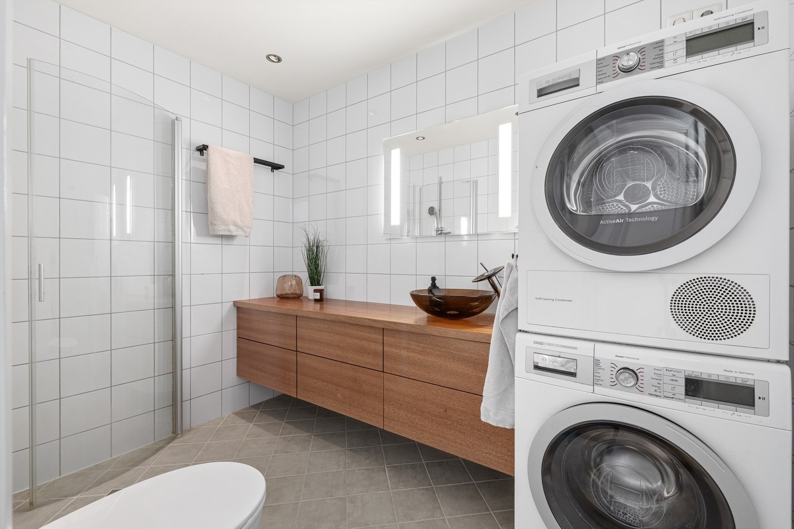 Flislagt bad inneholdende vegghengt toalett, innredning med servant og nydelig benkeplate som også er plassbygd, dusj/vegger og opplegg til vaskemaskin. Galleribilde