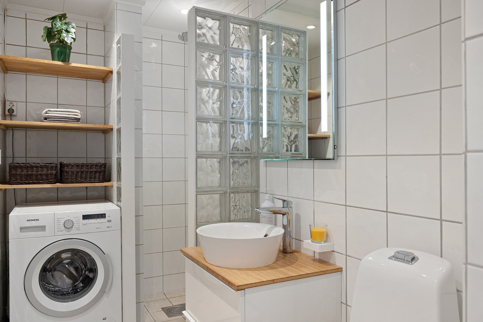 Badet har et gulvmontert toalett og et lekkert servantskap med skuffer i høyglans. Det er montert et speil med overlys som gir godt lys, det er også opplegg for vaskemaskin. Galleribilde