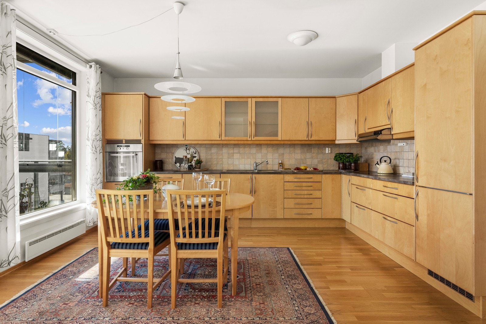 Kjøkkenet har en tidløs innredning med trefarget, glatte fronter, mørk benkeplate i laminat og integrerte hvitevarer. Galleribilde