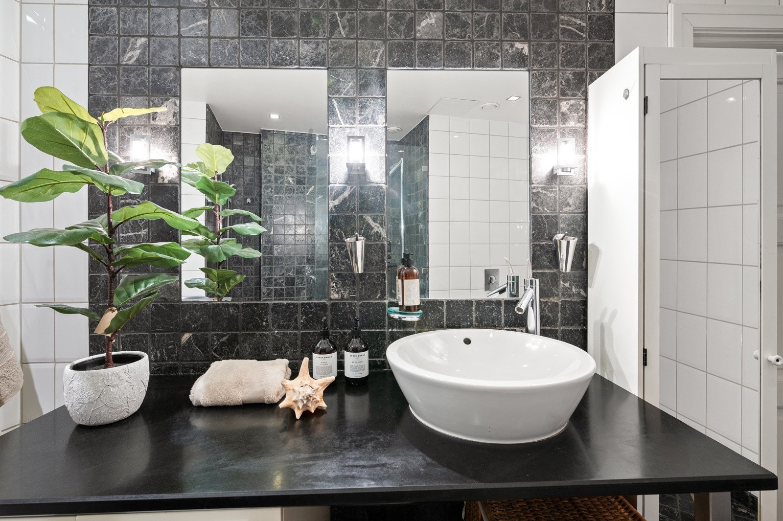 Rommet er kledd med hvite veggfliser som er smakfullt satt i kontrast til natursteinsfliser i sort. Galleribilde