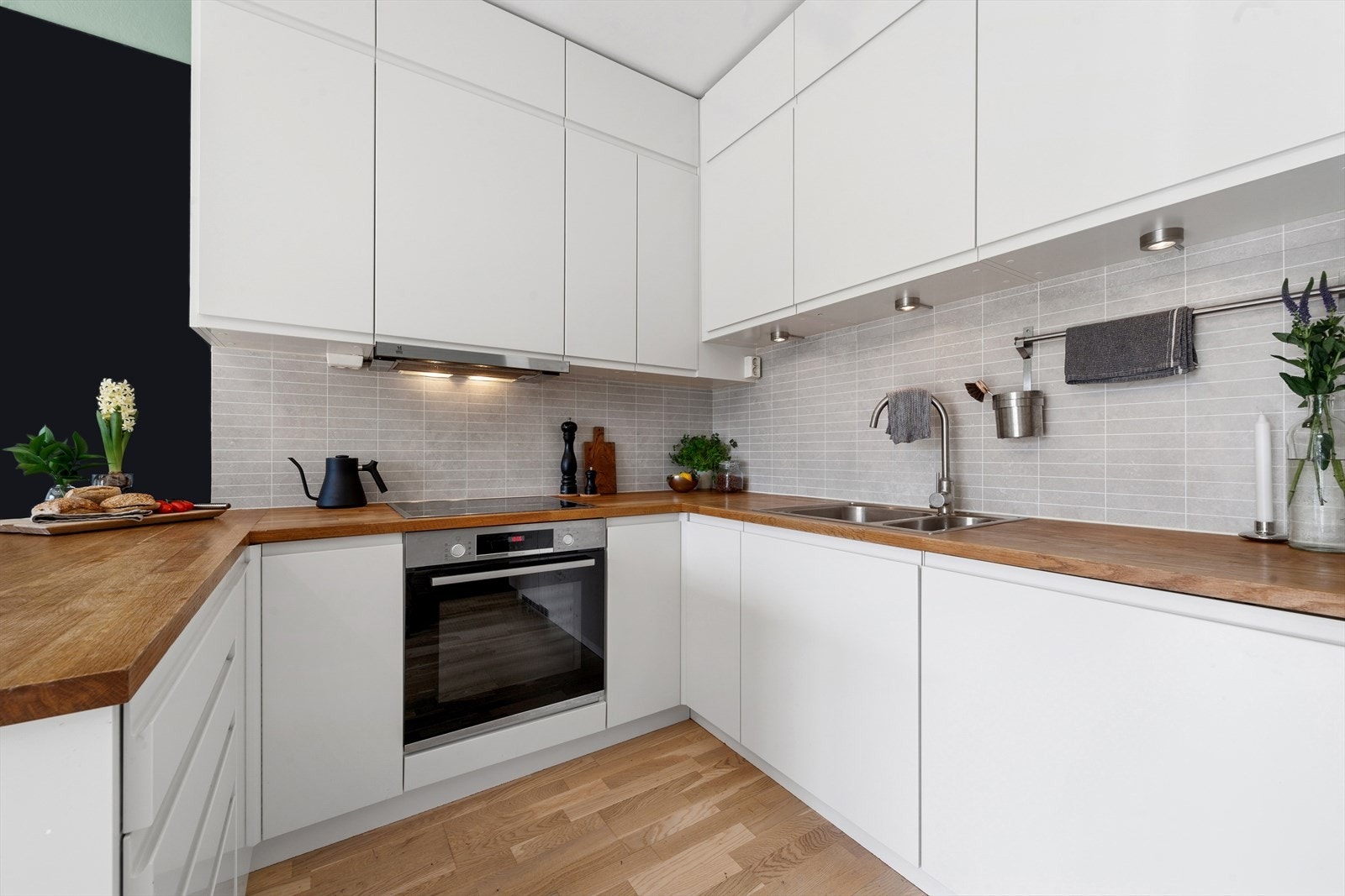 Kjøkkenet er innredet med glatte folierte fronter, benkeplate i tre med nedfelt kum i rustfritt stål og plater på vegg over benk Galleribilde