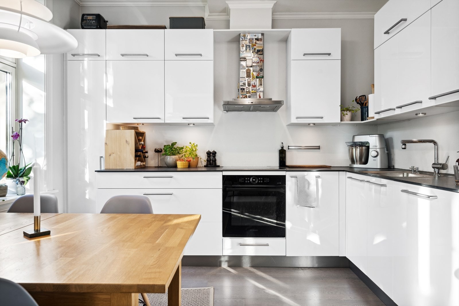 Moderne og stilrent kjøkken med hvite høyglansfronter og integrerte hvitevarer. Den åpne løsningen gir god plass til spisebord og skaper en lys og luftig atmosfære. Galleribilde