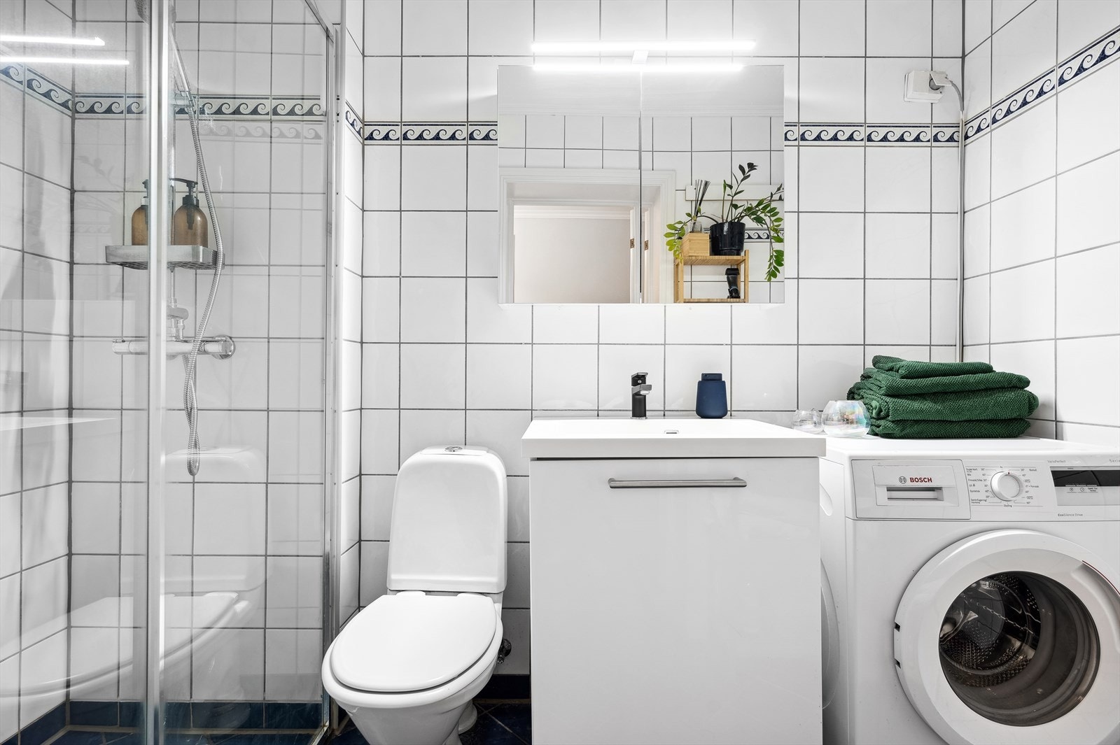 Lyst og funksjonelt bad med dusj, opplegg for vaskemaskin og praktisk oppbevaring. Galleribilde