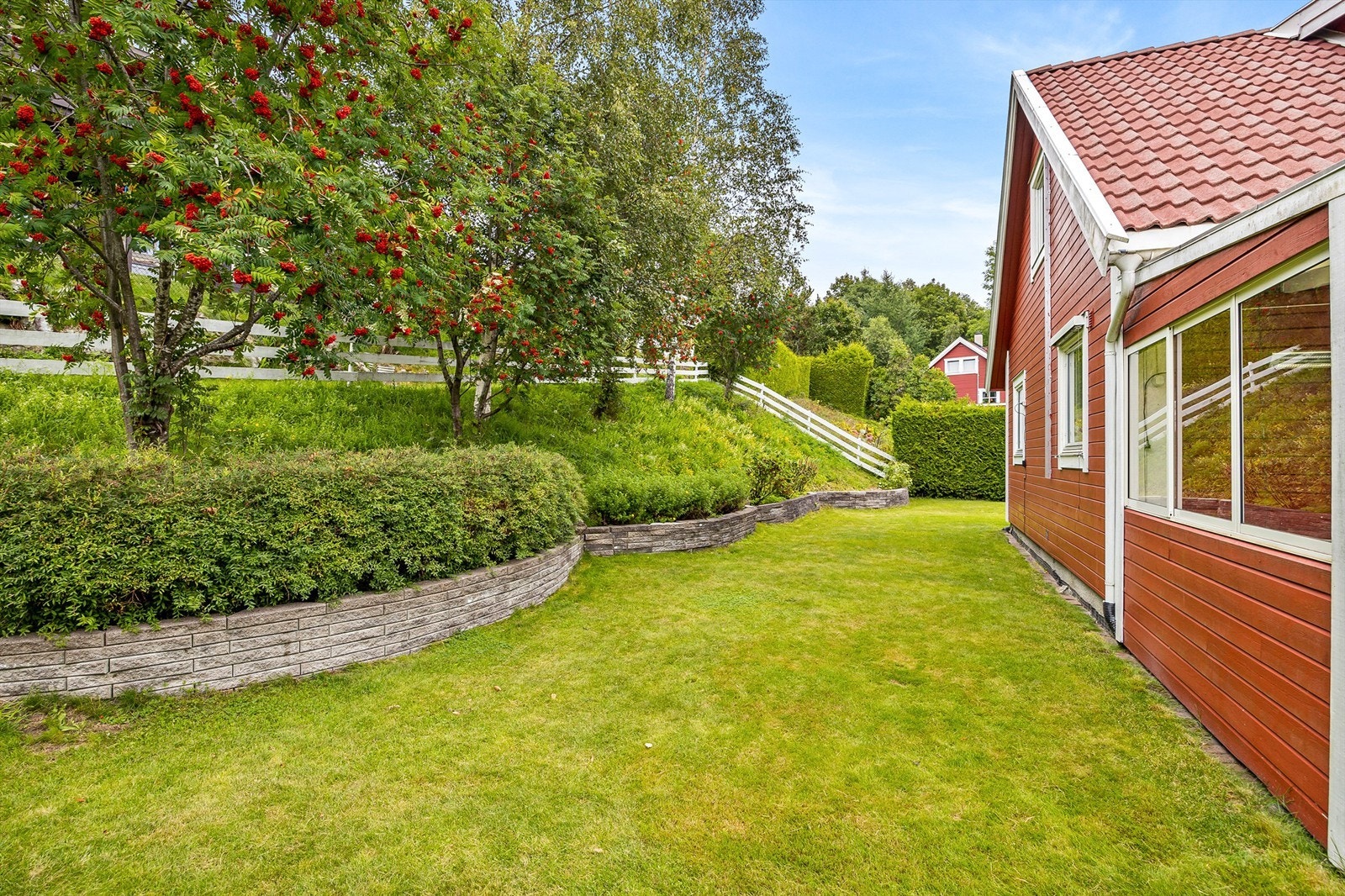 Variert hage med plen over flere nivåer/soner og skråning med blomsterbed samt trær som skjermer innsyn Galleribilde