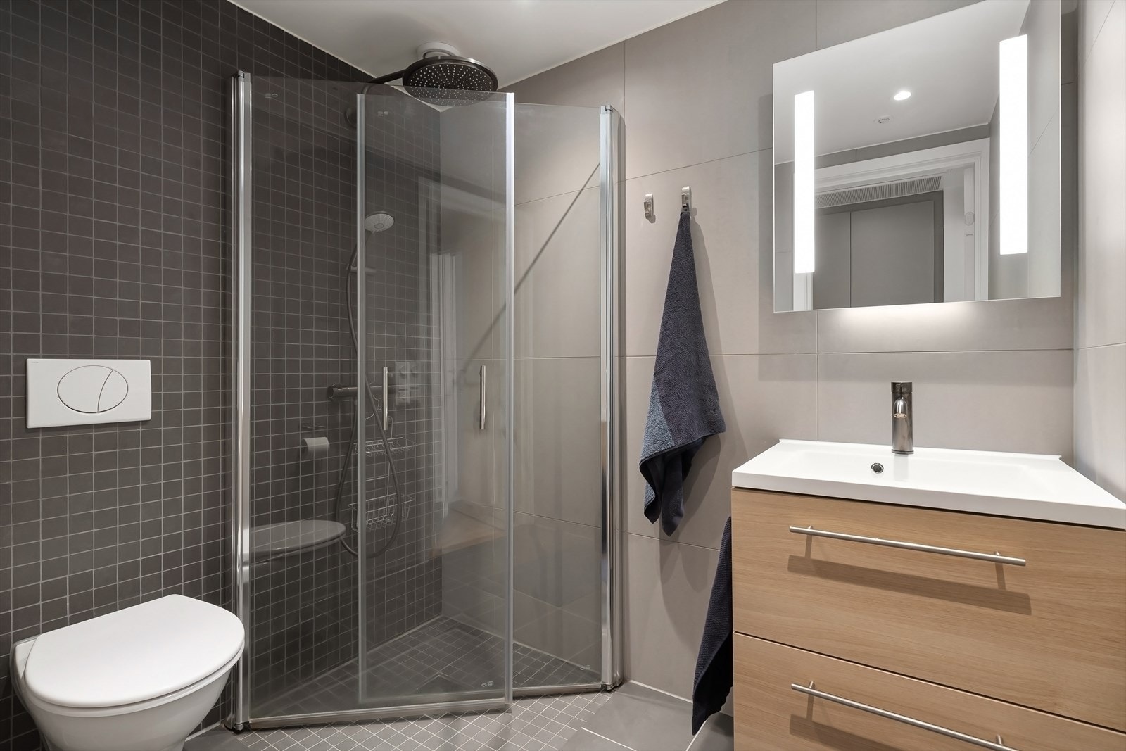 Bad 2 med nedsenket dusjhørne med dører i herdet glass, helservant med underskuffer, speil med LED lys over servant og vegghengt toalett. Galleribilde