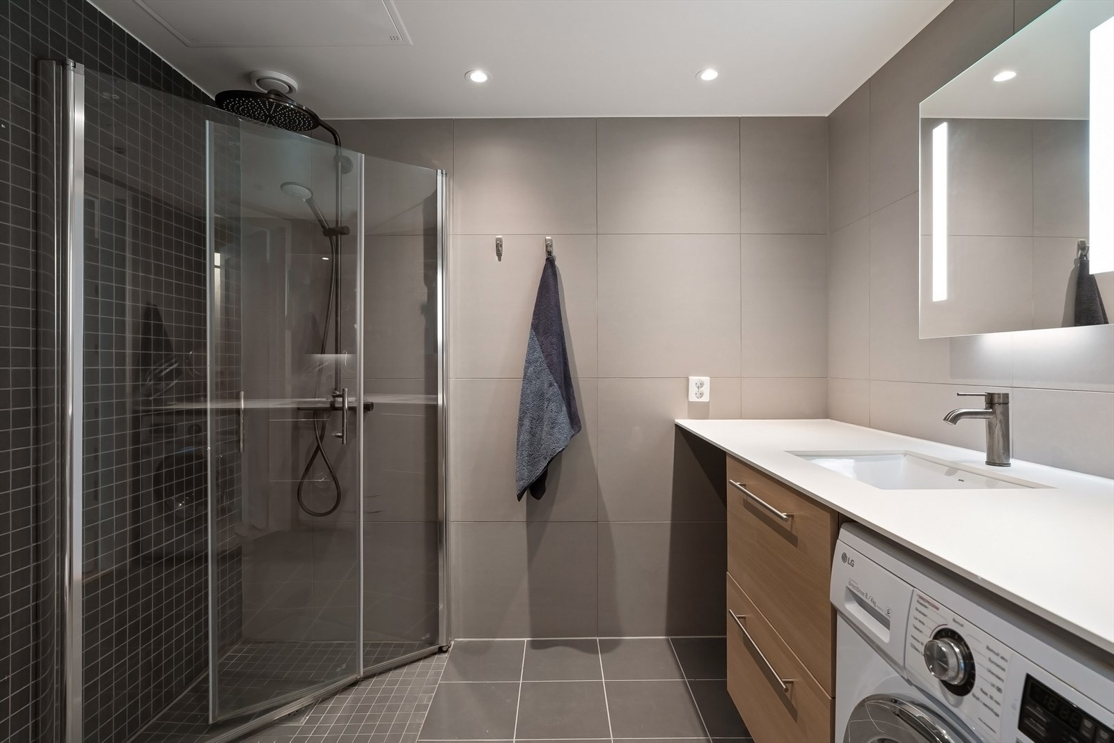 Bad 1 en-suite med senket dusjhørne med dører i herdet glass, benkeplate med underlimt servant, underskuffer og tilpasset plass for vaskemaskin og tørketrommel. Galleribilde