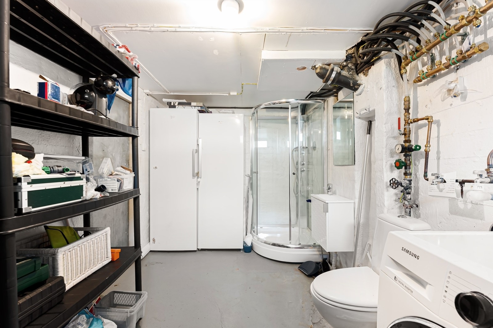 Vaskerom med støpt gulv, malte betongvegger, malt himling, toalett, vegghengt servantskap med ovenpåliggende servant og opplegg for vaskemaskin og tørketrommel Galleribilde